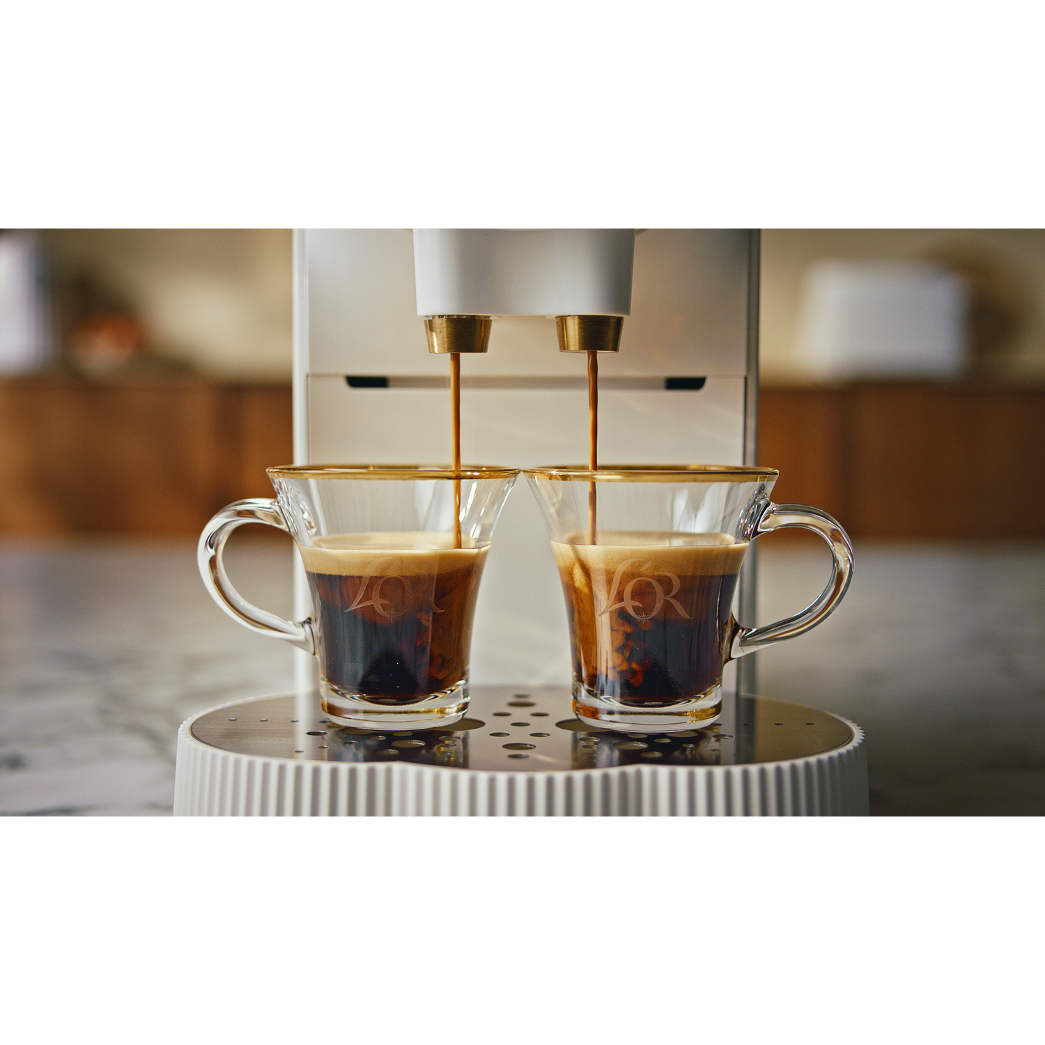 Twee doorzichtige glazen met gouden randen, koffie die uit de machine stroomt.