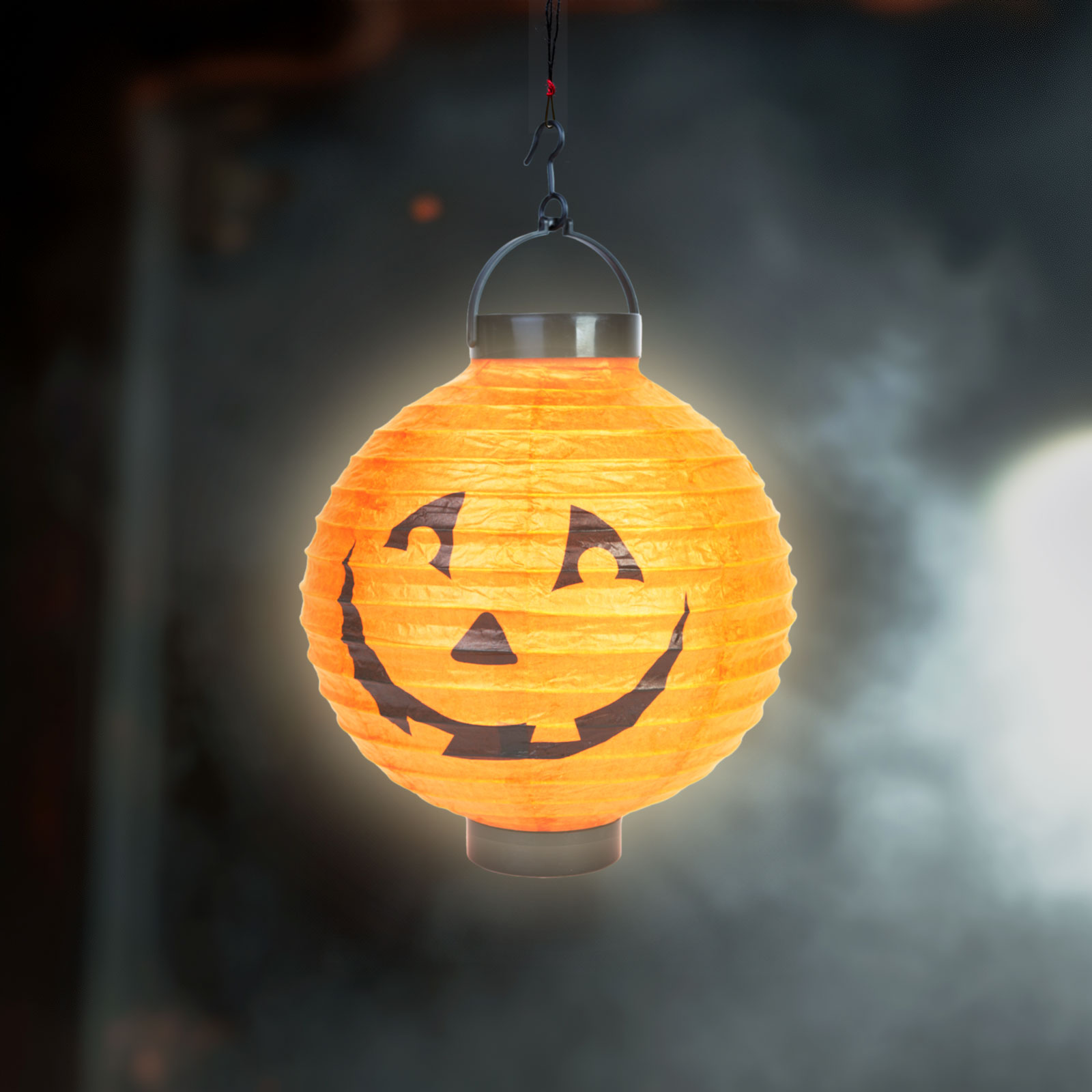 Narancssárga Halloween lámpás mosolygó arccal, fekete háttérben lóg.