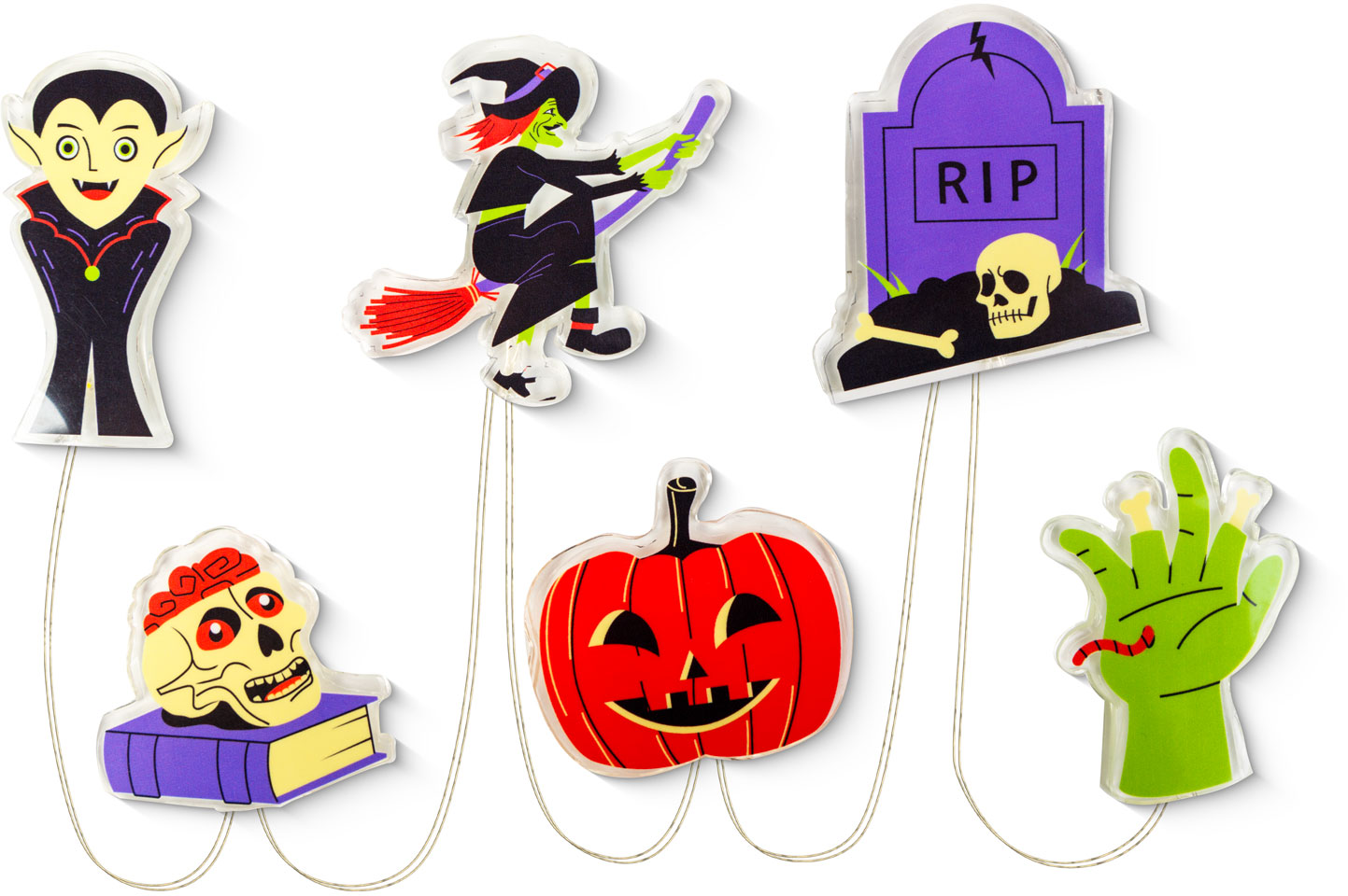 Halloween dekorációk: egy vámpír, egy boszorkány, egy sírkő, egy koponya egy könyvön, egy tök és egy zöld kéz.