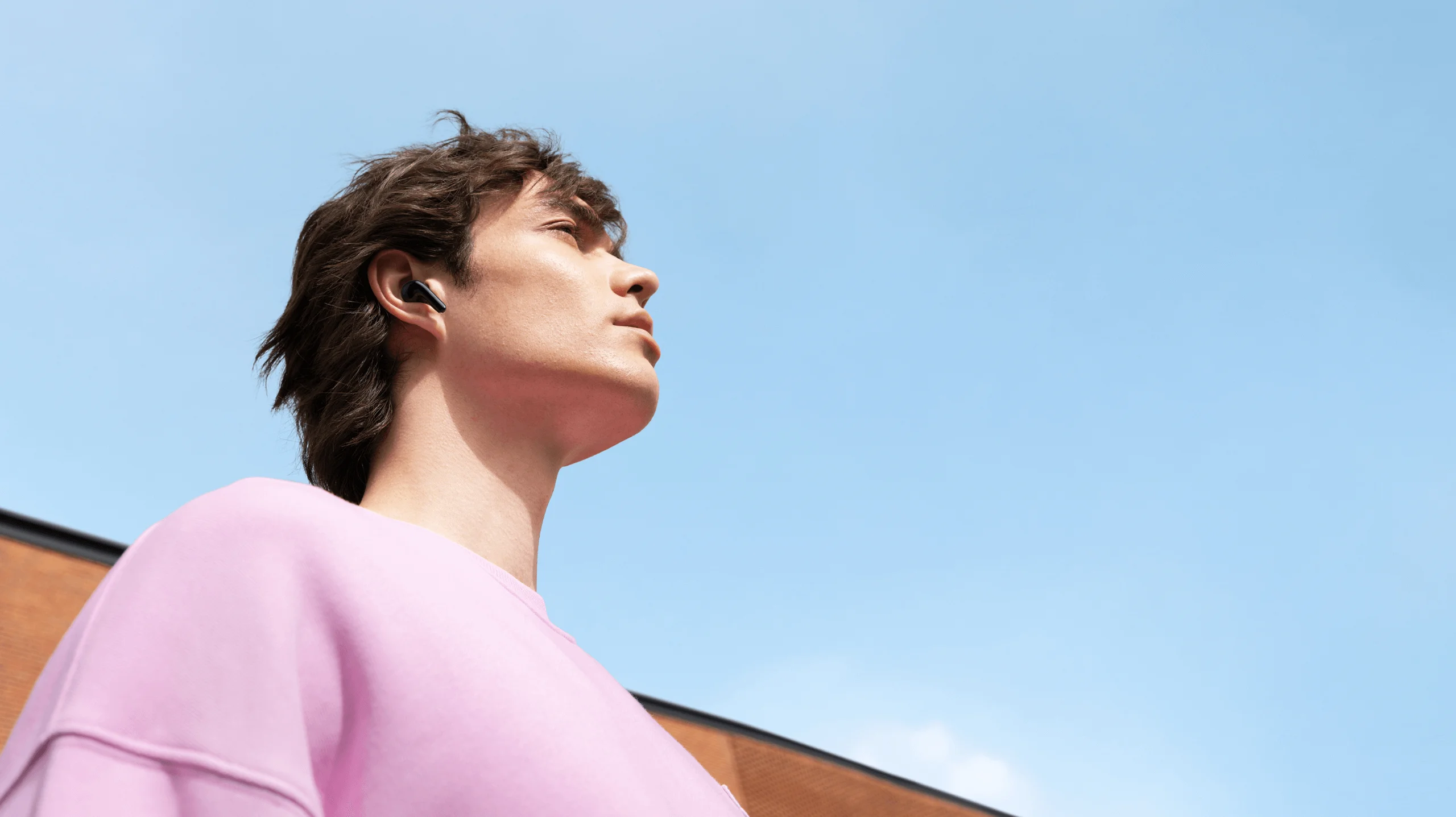 Homme portant des écouteurs, regardant le ciel. Il porte un pull rose.