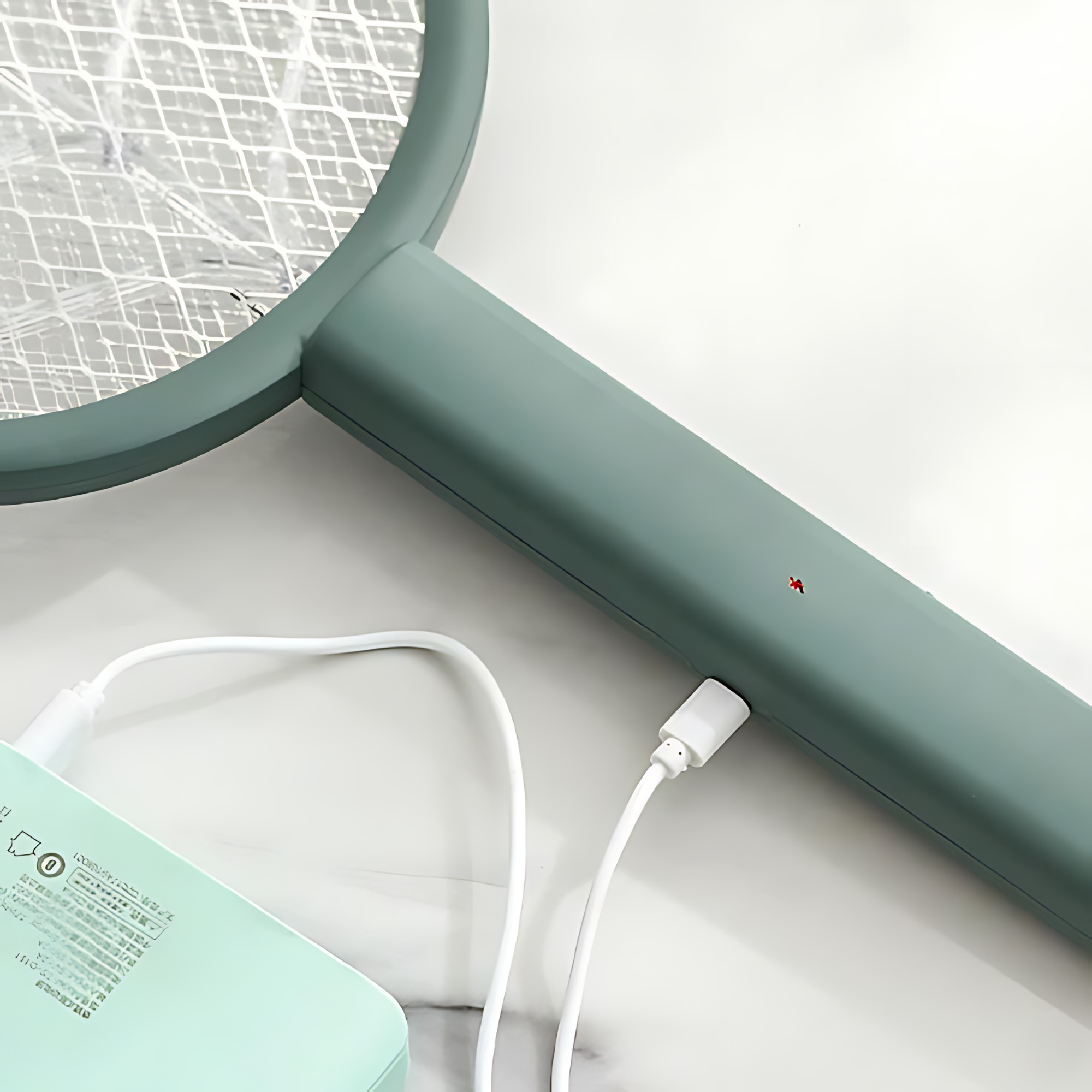 Zielona elektryczna packa na muchy z białym kablem ładującym. Leży na białej powierzchni.