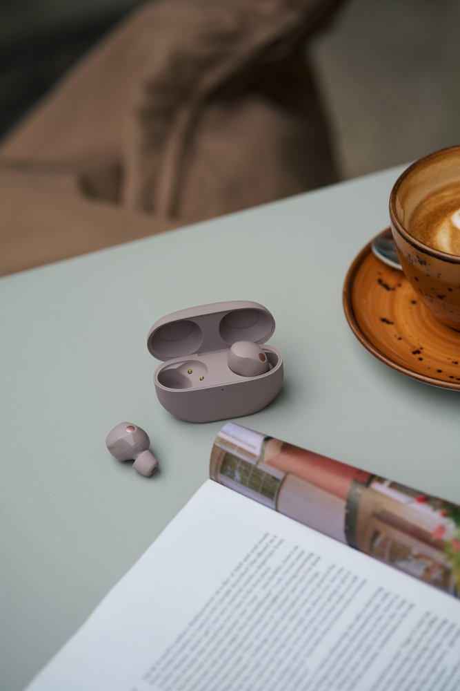 Écouteurs sans fil dans un étui et un seul écouteur sur une table avec un magazine et du café.