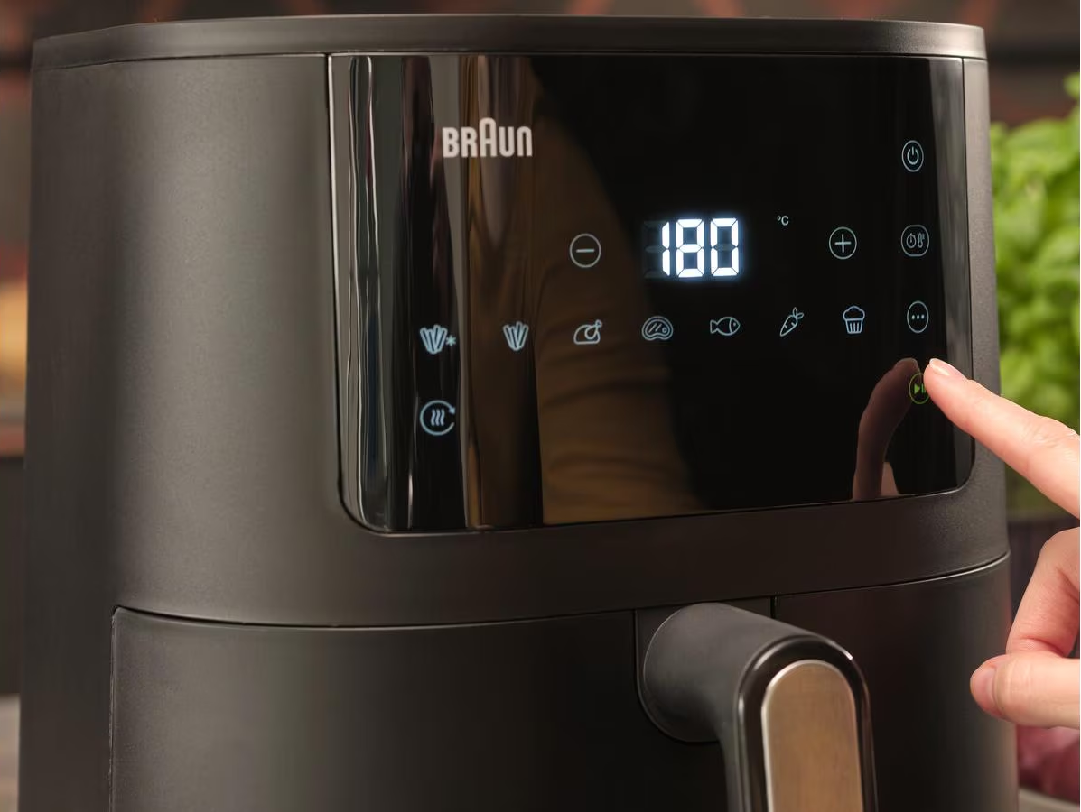 Friggitrice ad aria Braun nera con display digitale 180°C. Una mano preme un pulsante.
