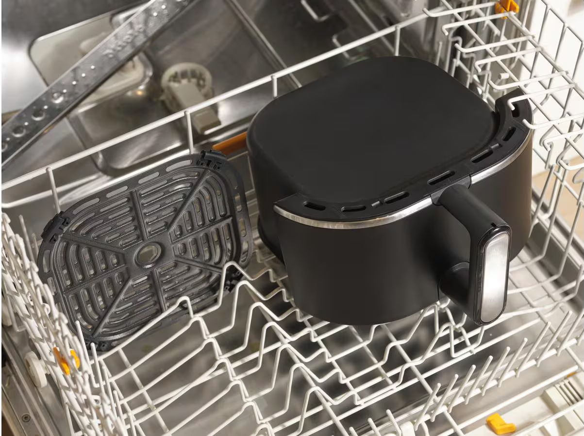 Friggitrice ad aria nera con il suo cestello e un vassoio grill all'interno di una lavastoviglie.