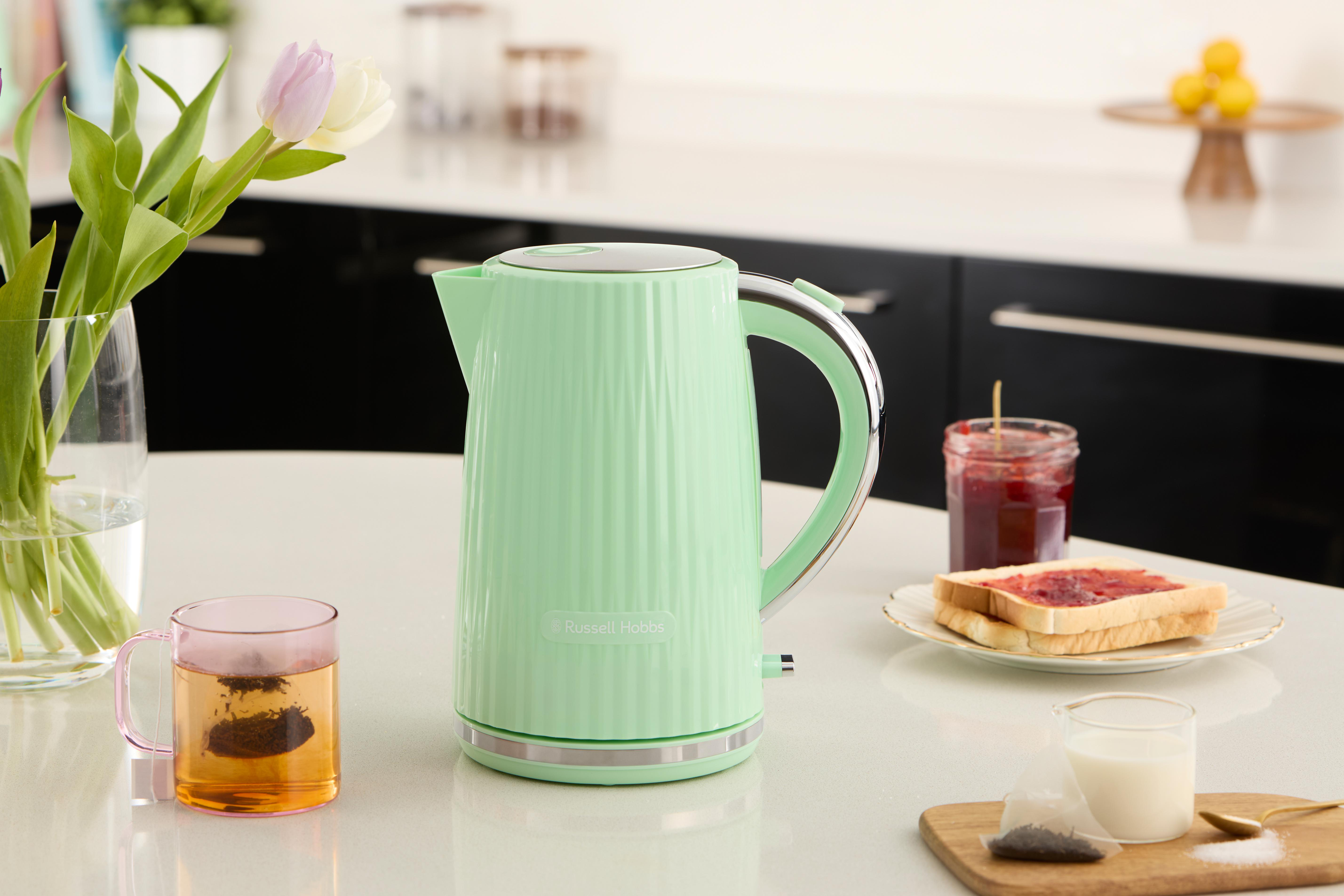 Ein mintgrüner Russell Hobbs Wasserkocher auf einem Tisch mit Tee, Marmelade und Blumen.