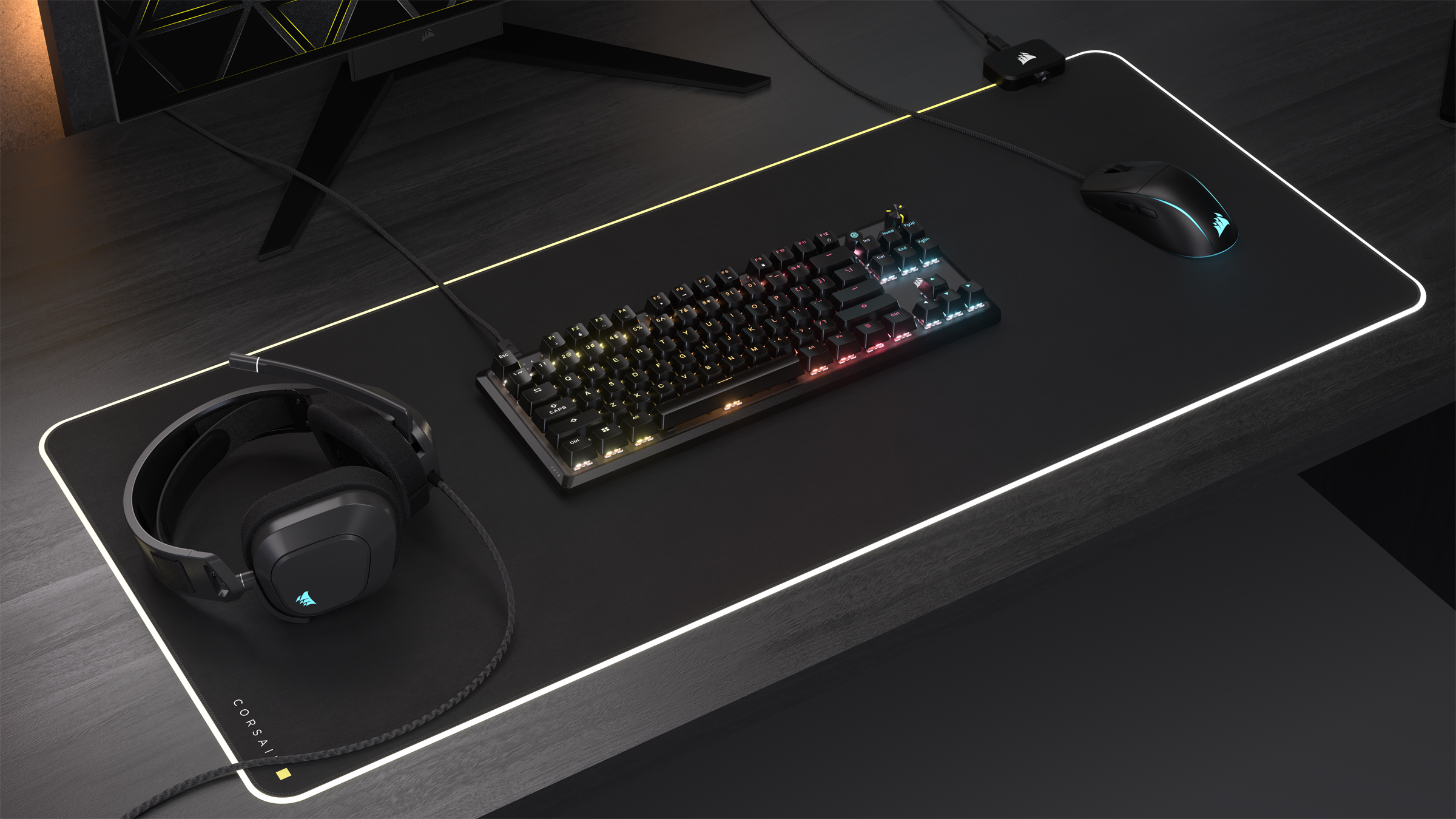 Configurazione di gioco: tastiera, mouse e cuffie su un tappetino nero. Monitor sullo sfondo.