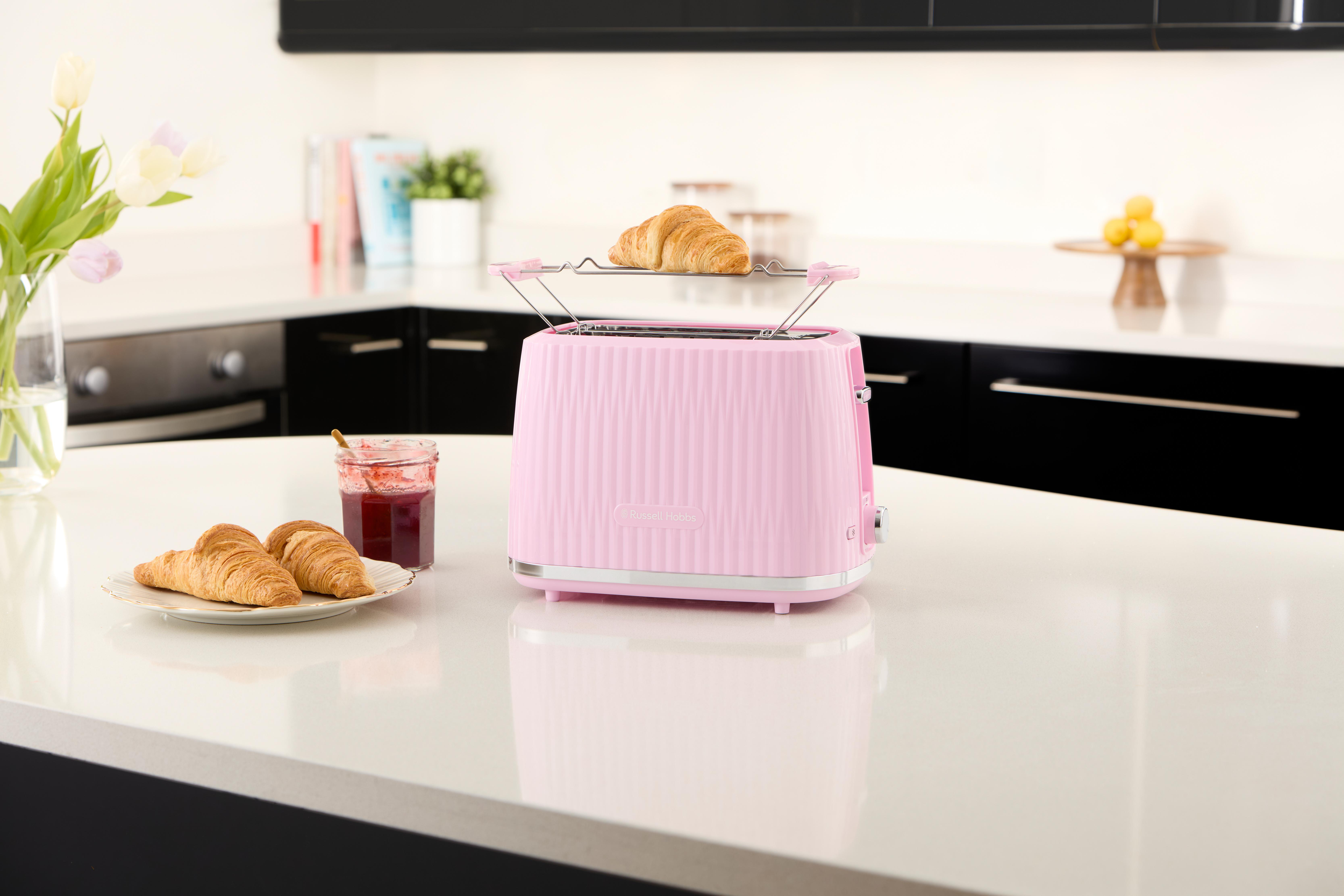 Rosa Toaster mit Croissants und Marmeladenglas auf weißer Arbeitsplatte.
