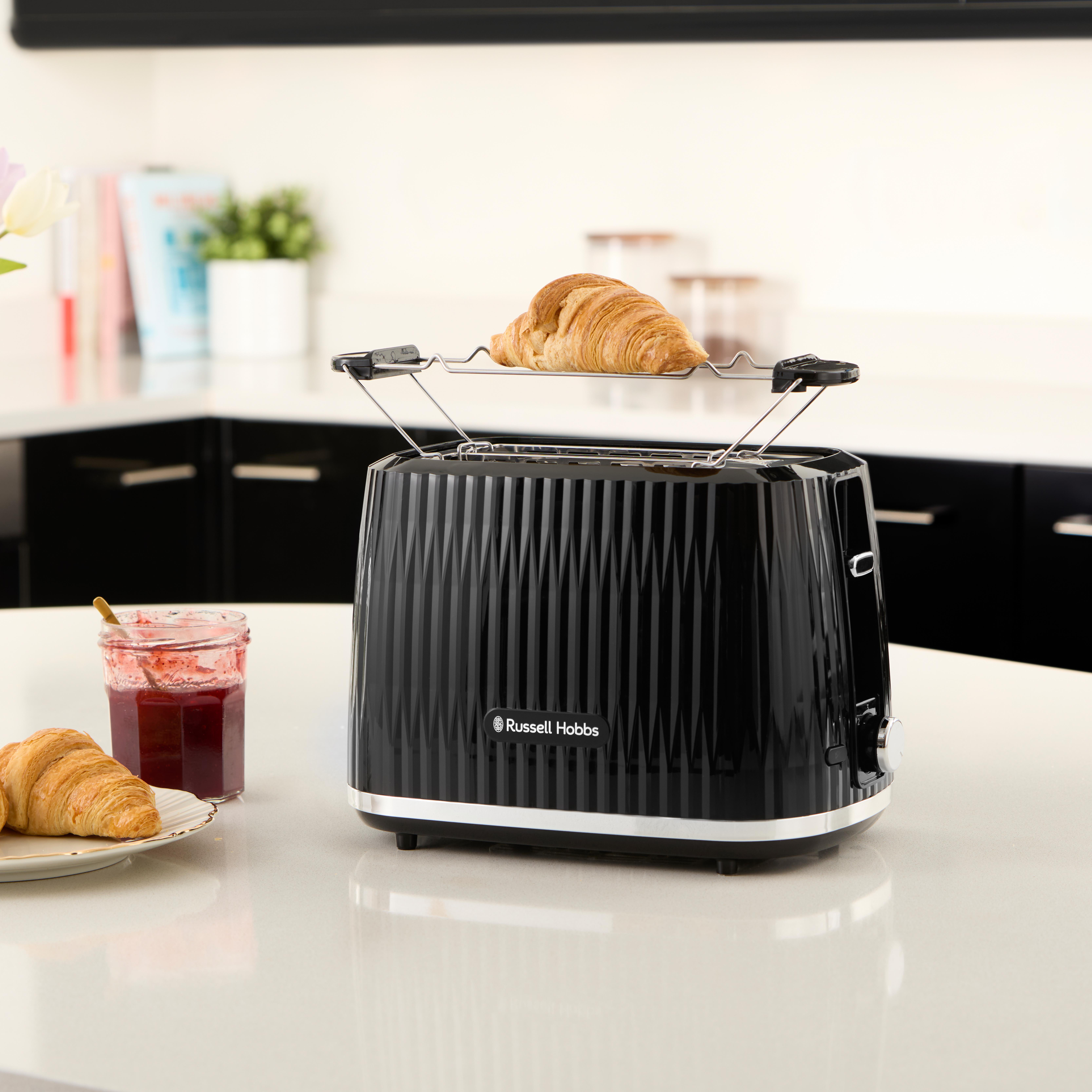Schwarzer Toaster mit Croissant im Gestell. Ein Glas Marmelade und ein weiteres Croissant daneben.