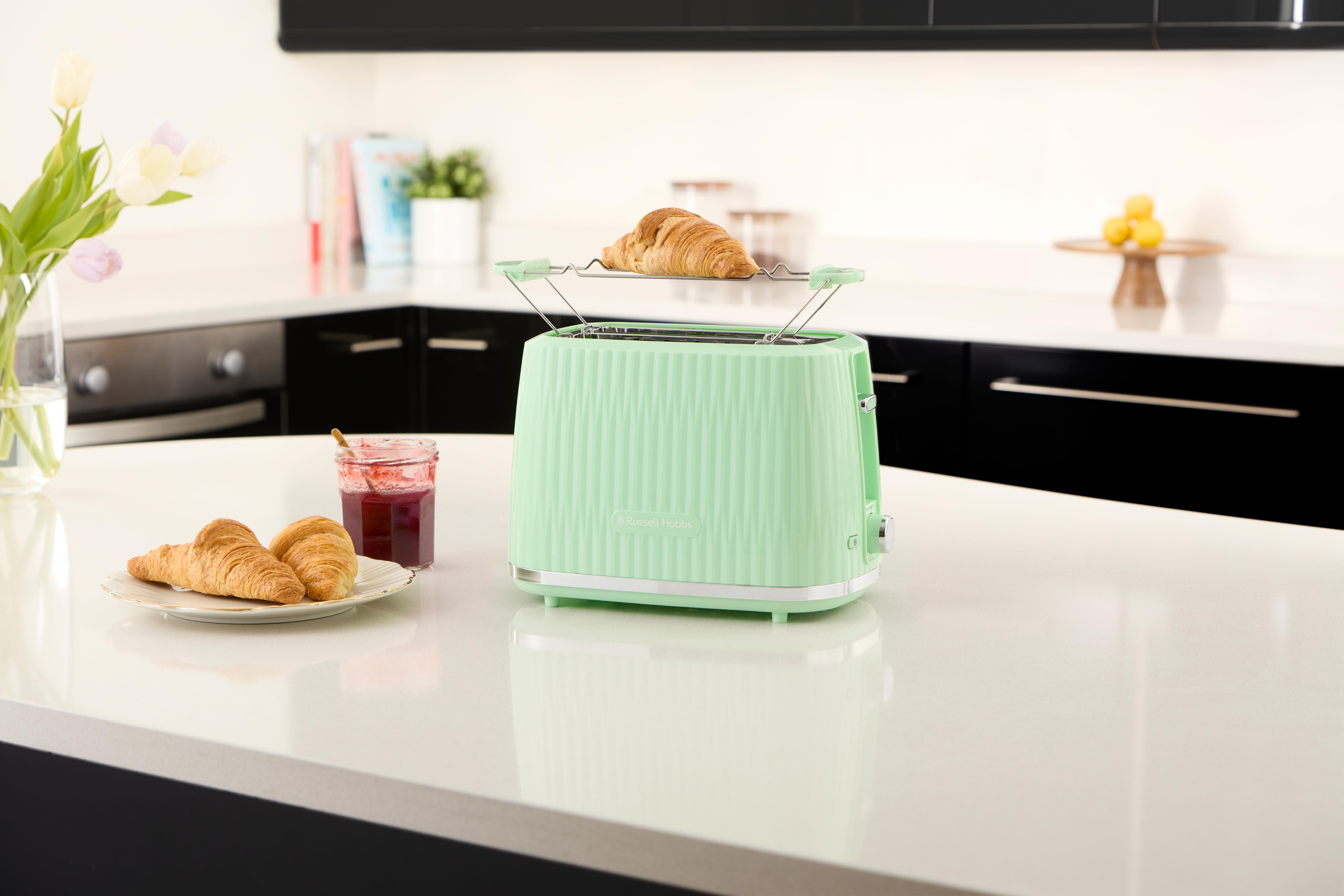 Minzgrüner Toaster mit Croissants und Marmelade auf weißer Theke.