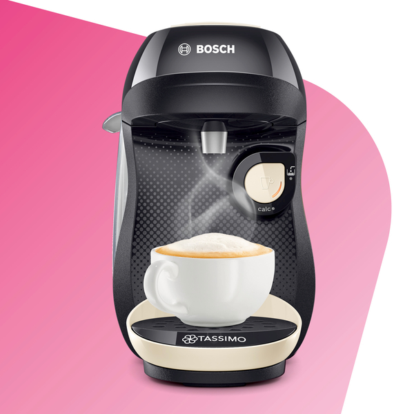 Schwarze und cremefarbene Tassimo-Kaffeemaschine mit einer Tasse Kaffee auf rosa Hintergrund.