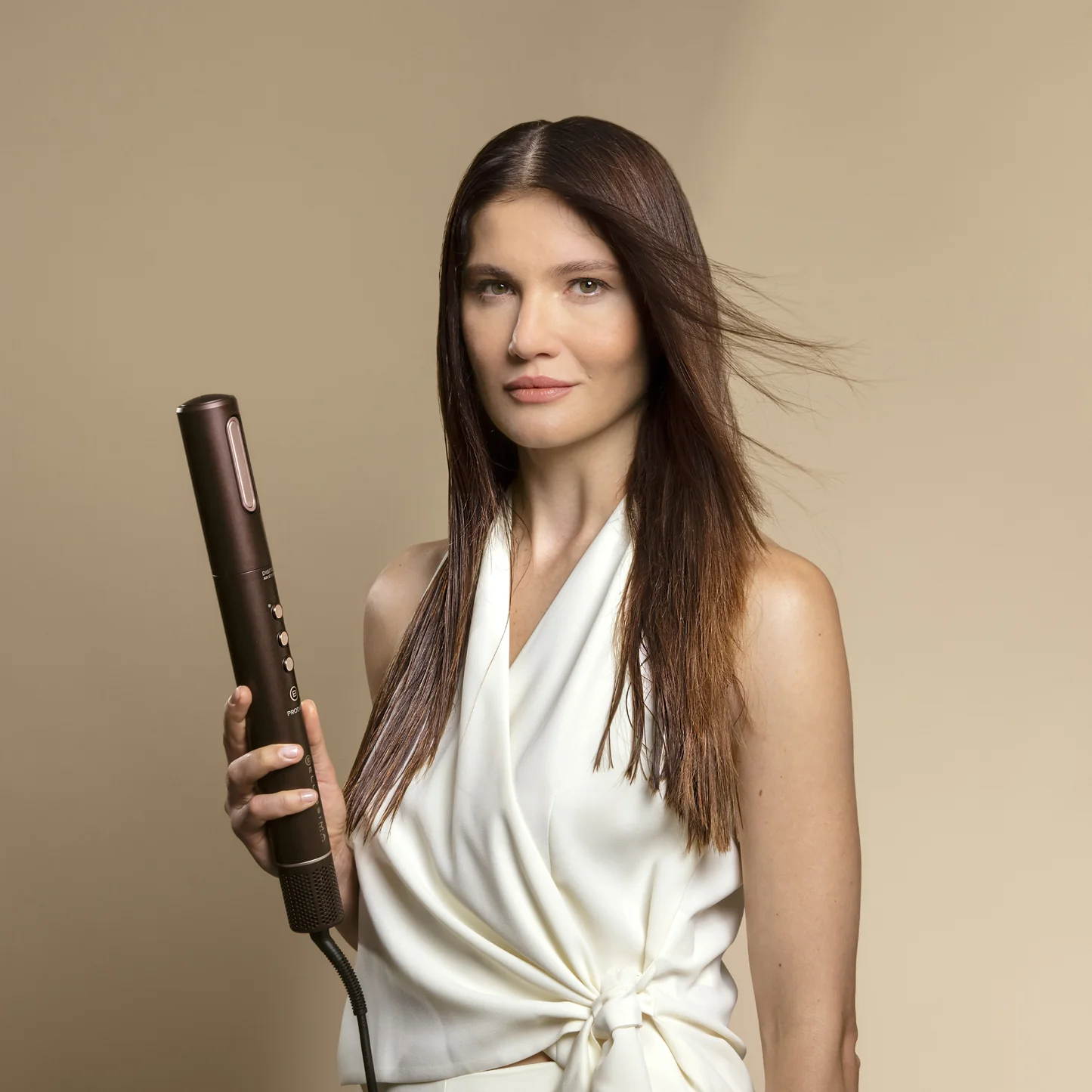 Una donna che tiene un arricciacapelli marrone. Ha lunghi capelli castani.