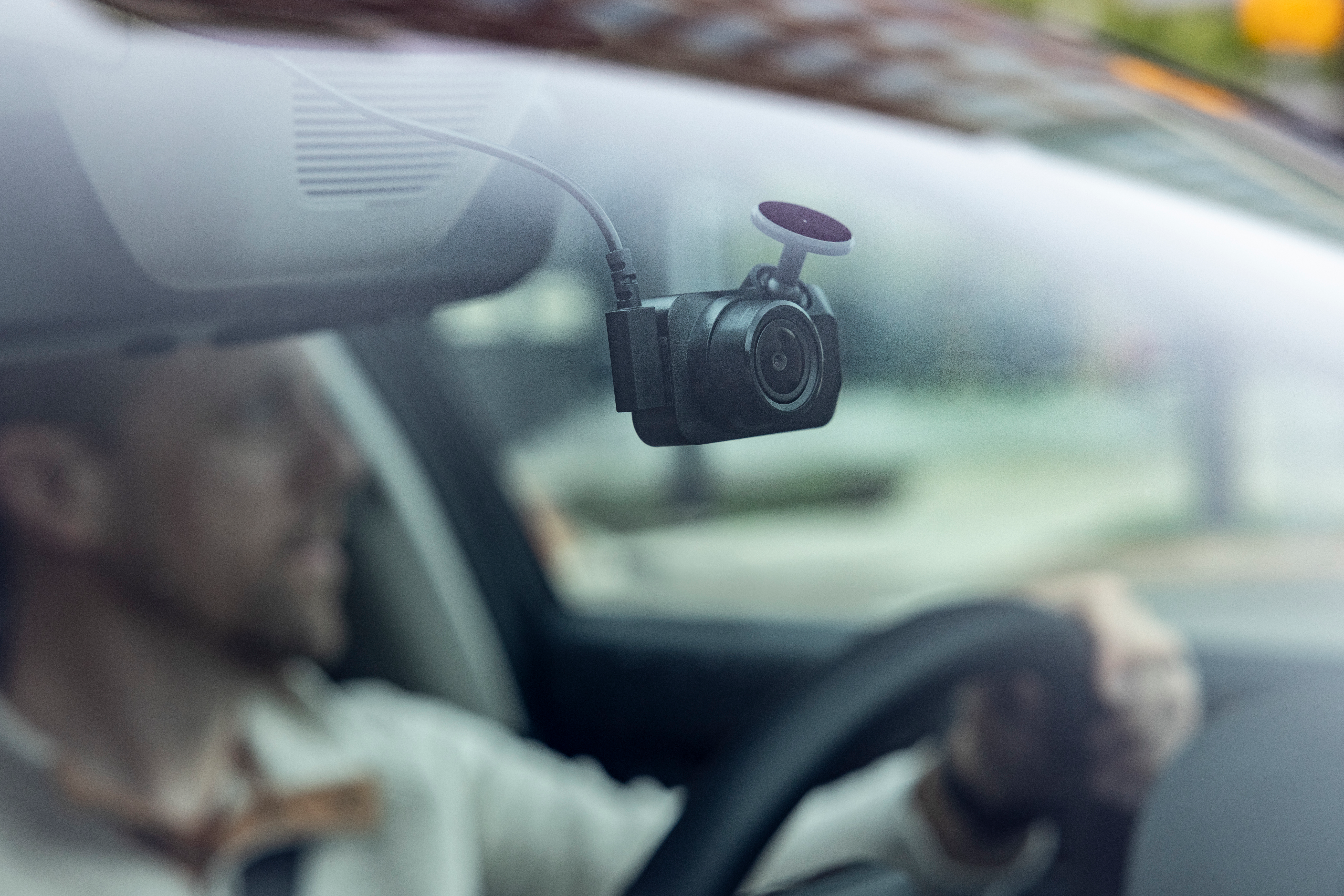 Une caméra de bord noire montée sur le pare-brise d'une voiture, une personne conduisant en arrière-plan flou.