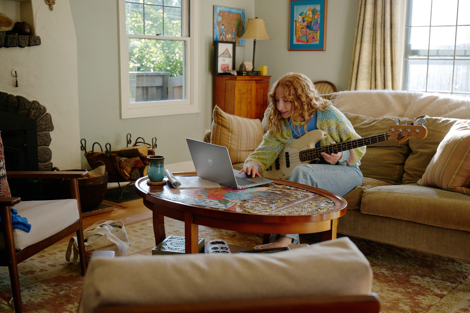 Vrouw speelt basgitaar in een woonkamer met een laptop op een tafel.