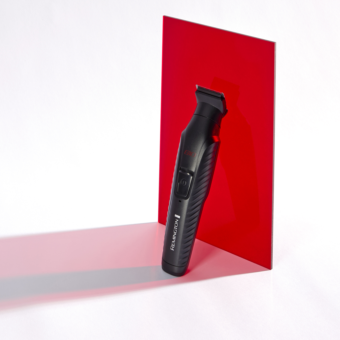 Fekete Remington trimmer egy piros panel előtt, fehér felületen. A trimmer árnyékot vet.