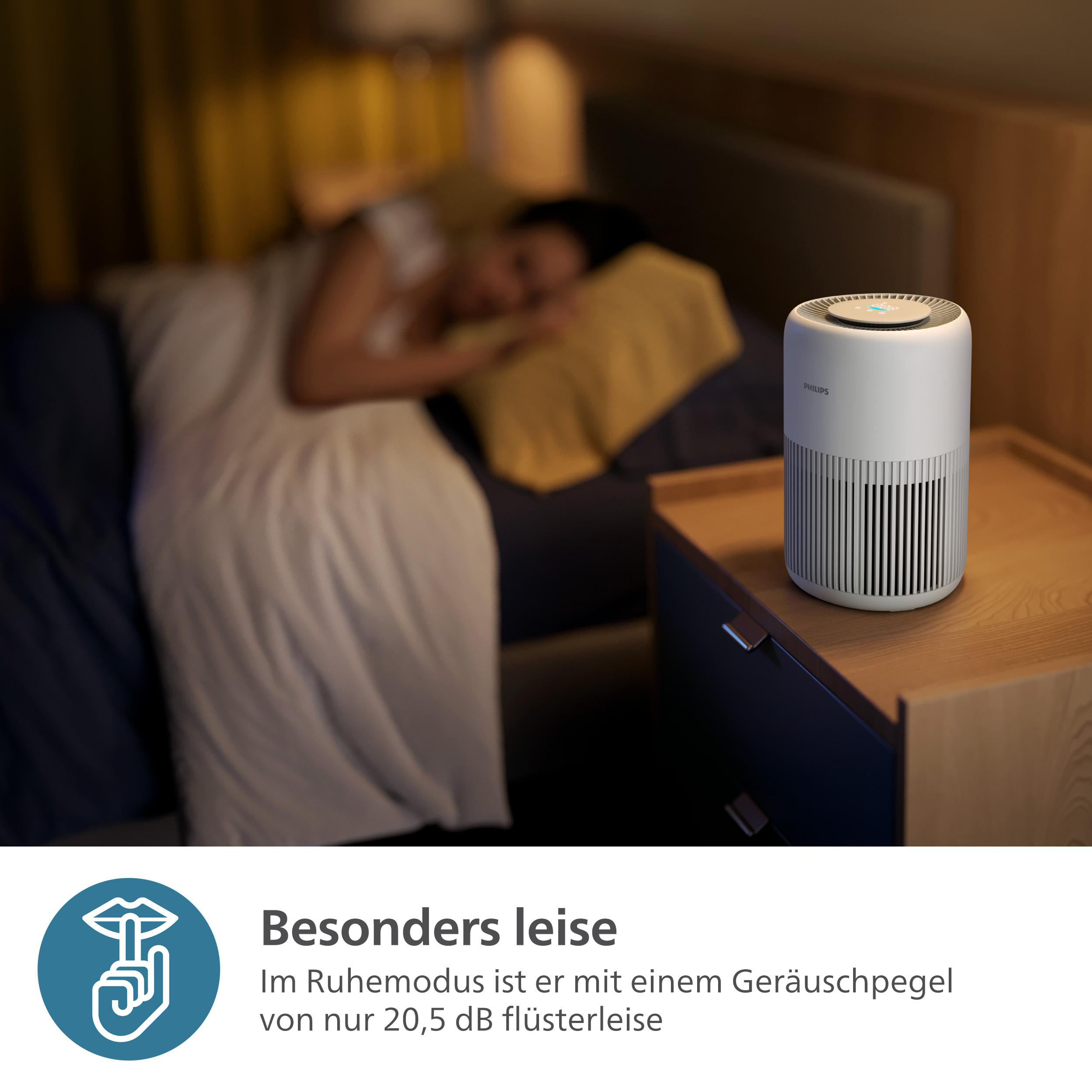 Eine Person schläft im Bett, neben einem Luftreiniger auf einem Nachttisch. Text auf Deutsch.
