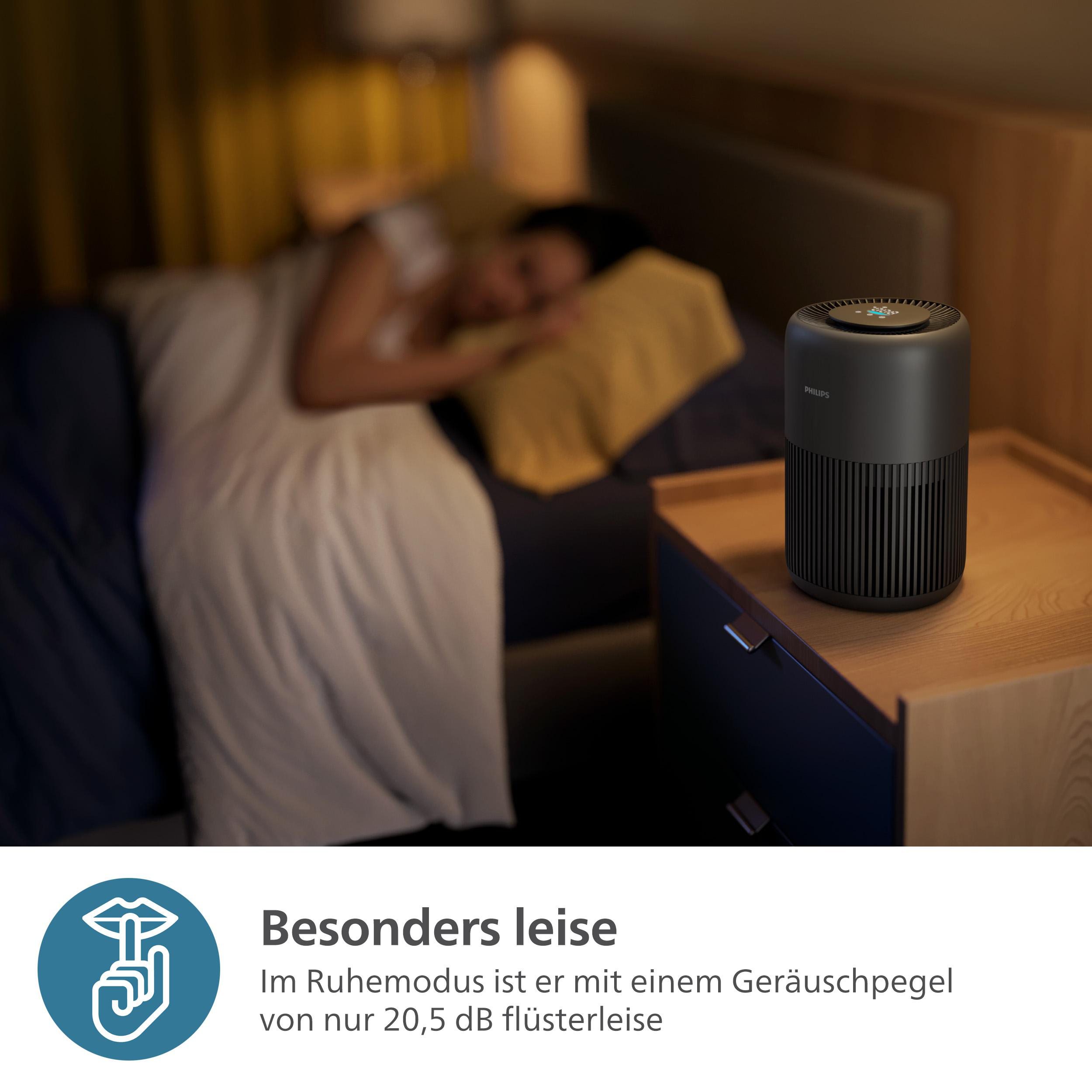 Luftreiniger auf Nachttisch, Person schläft im Bett, dunkle Raumeinstellung, in der Nähe eines Fensters.