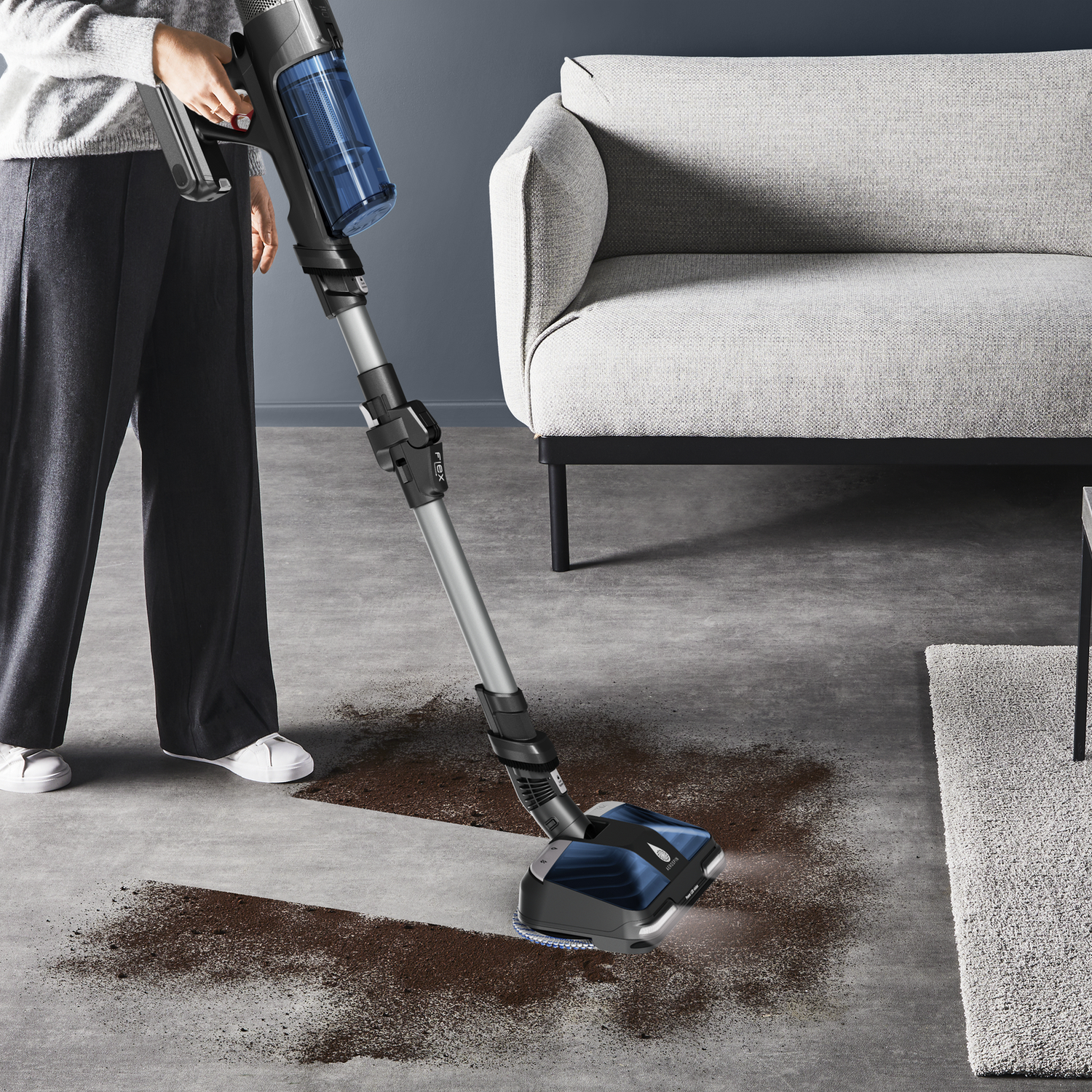 Woman using a black and blue vacuum cleaner on a floor with dirt.