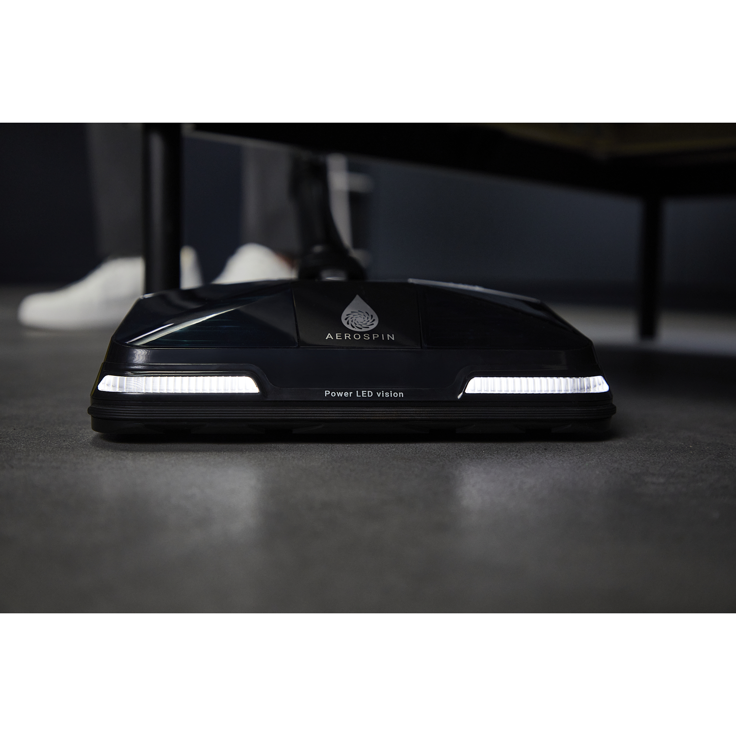 Black vacuum head with LED lights on a gray floor.