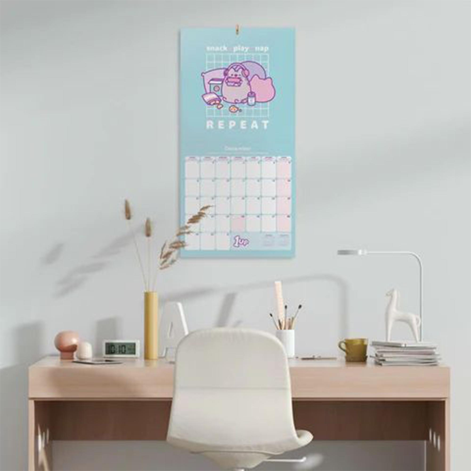Ein Wandkalender mit Cartoon-Grafik über einem Raster und einem Schreibtischaufbau.