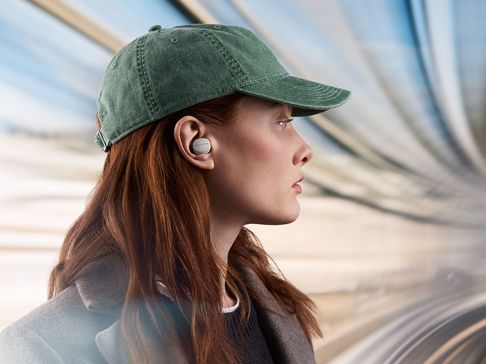 Kobieta z rudymi włosami w zielonej czapce i białych słuchawkach. Rozmyte tło.