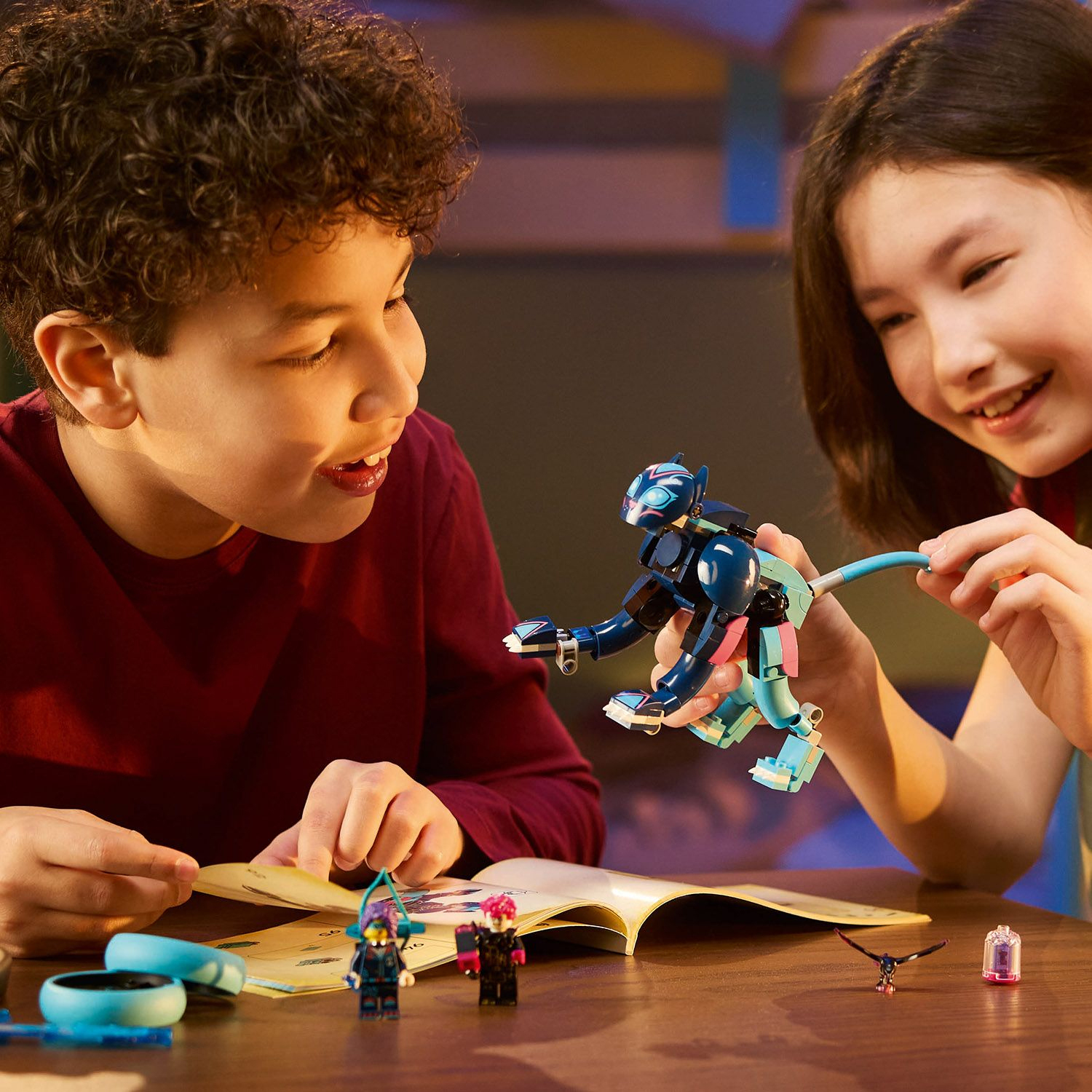 Due bambini costruiscono un modello Lego. Una creatura blu e rosa simile a un gatto viene assemblata.