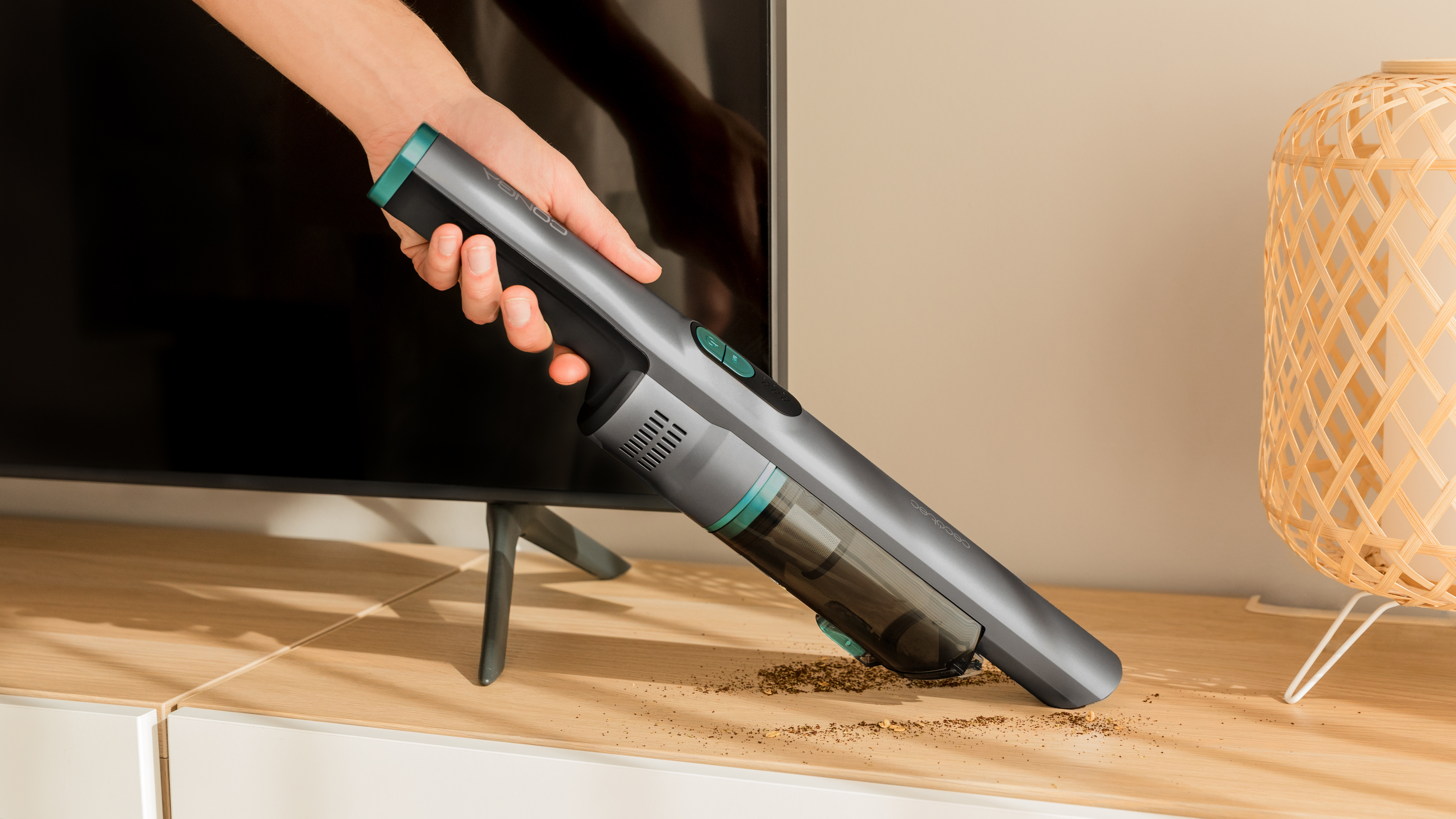 Una persona usando una aspiradora inalámbrica gris y verde sobre una superficie de madera, limpiando migas.