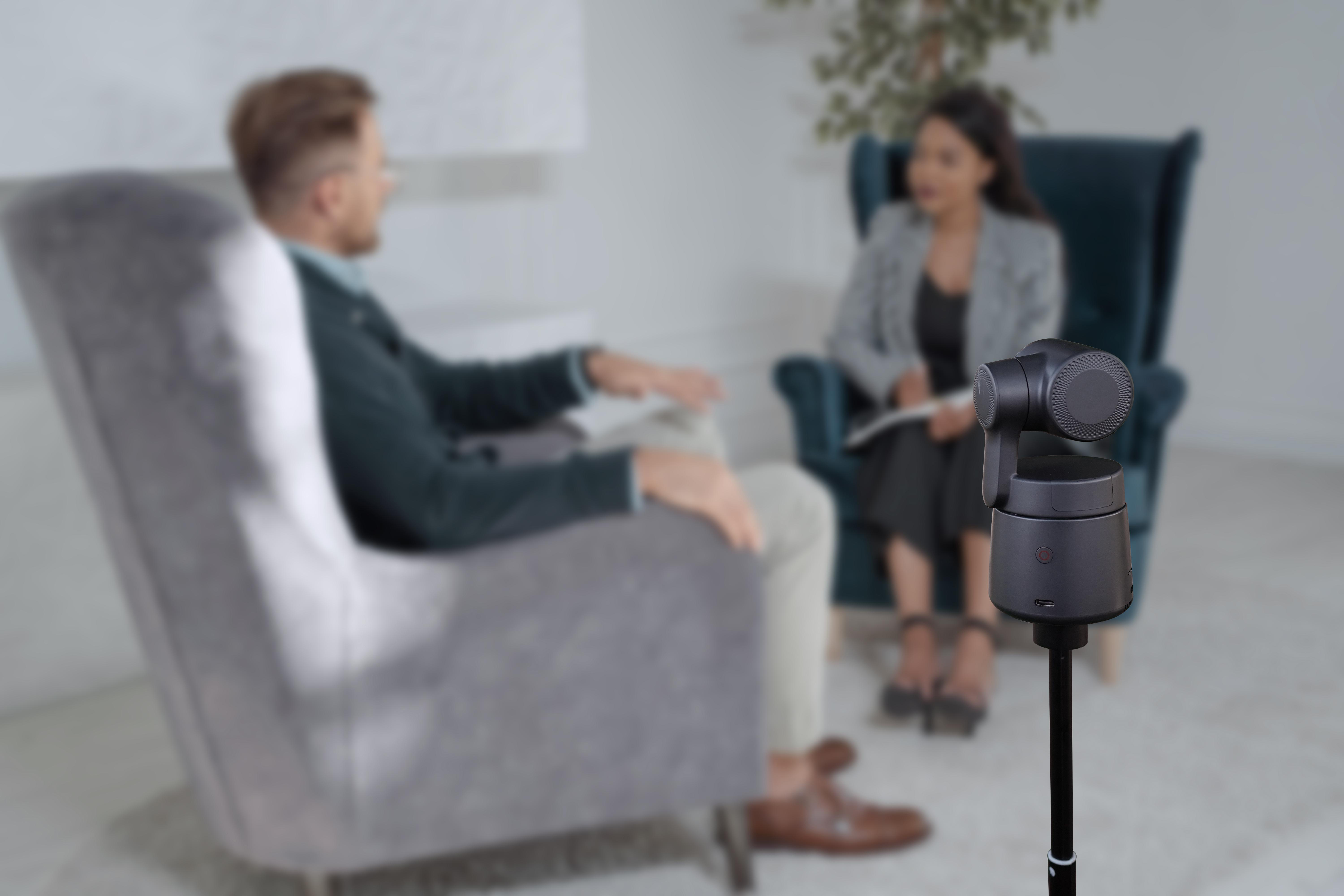 Eine Person in einem Interviewraum, mit einer Kamera auf einem Ständer im Vordergrund.