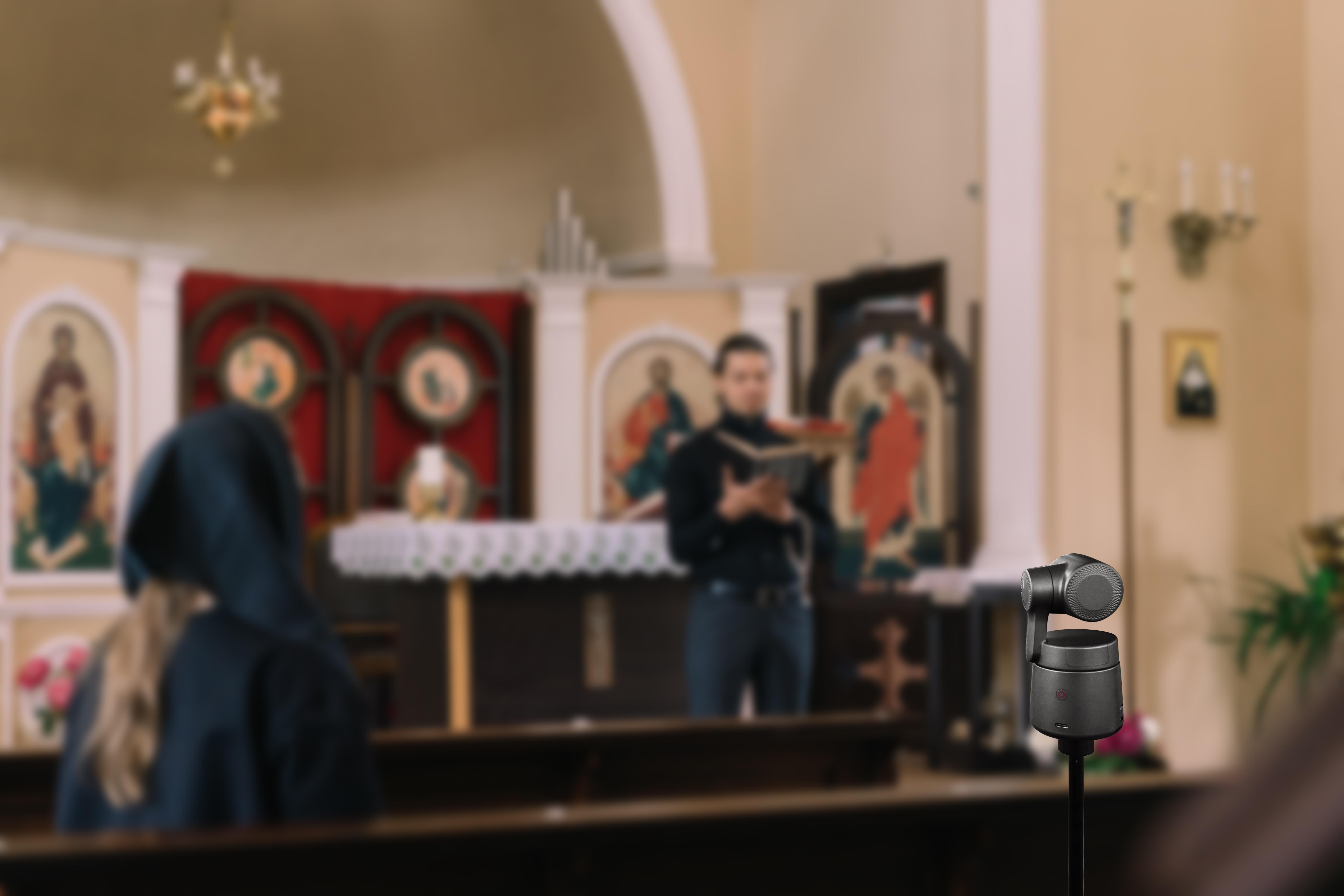 Ein Mikrofon in einer Kirche, mit verschwommenen Personen und religiösen Figuren im Hintergrund.