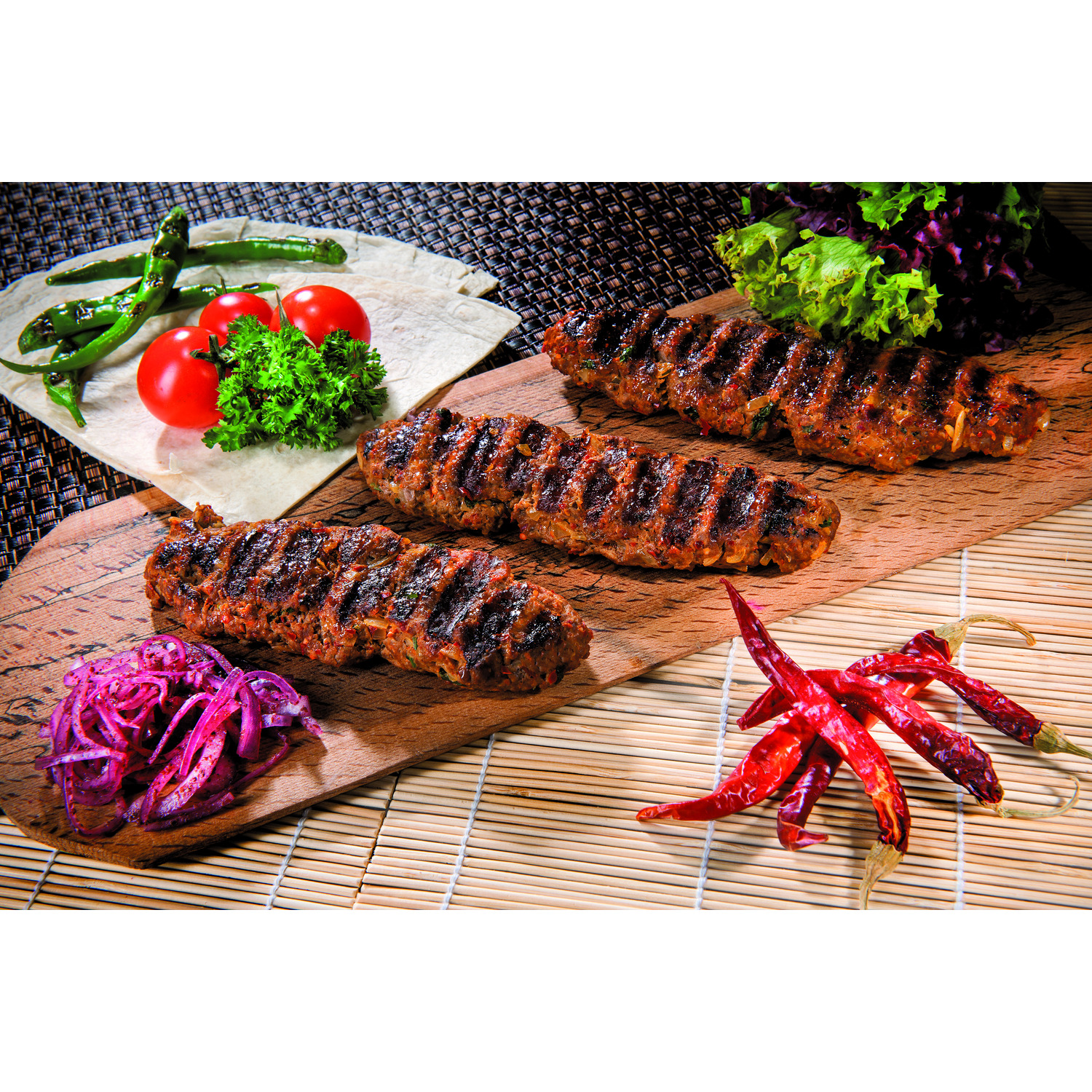 Kebabs grillés sur planche de bois avec tomates, poivrons et oignons rouges.