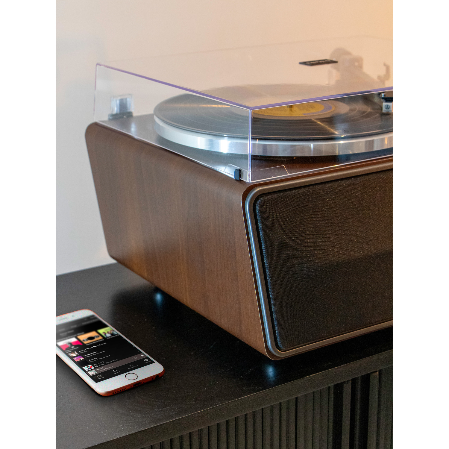 A turntable on a wooden cabinet with a smartphone showing a music app. A record is on the turntable.