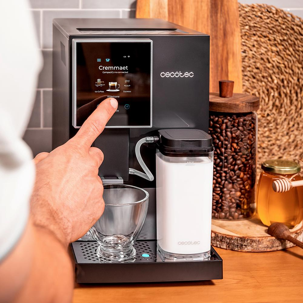 Persona tocando la pantalla de una cafetera, con un recipiente de leche y un tarro de miel detrás.