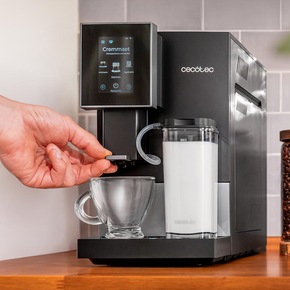 Cafetera negra con pantalla táctil, recipiente de leche y una taza de vidrio.