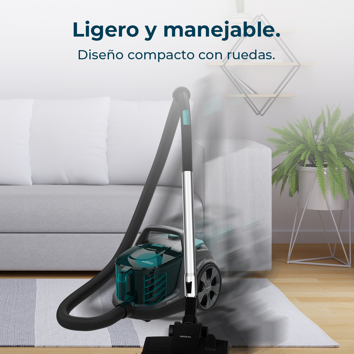 Una aspiradora está sobre una alfombra gris en una sala de estar. Se ven un sofá y plantas.