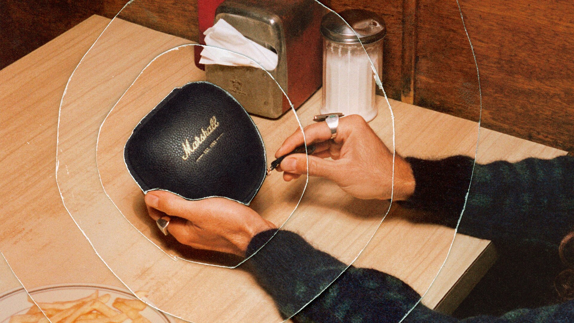 Personne ouvrant un étui d'écouteurs Marshall noir sur une table en bois.