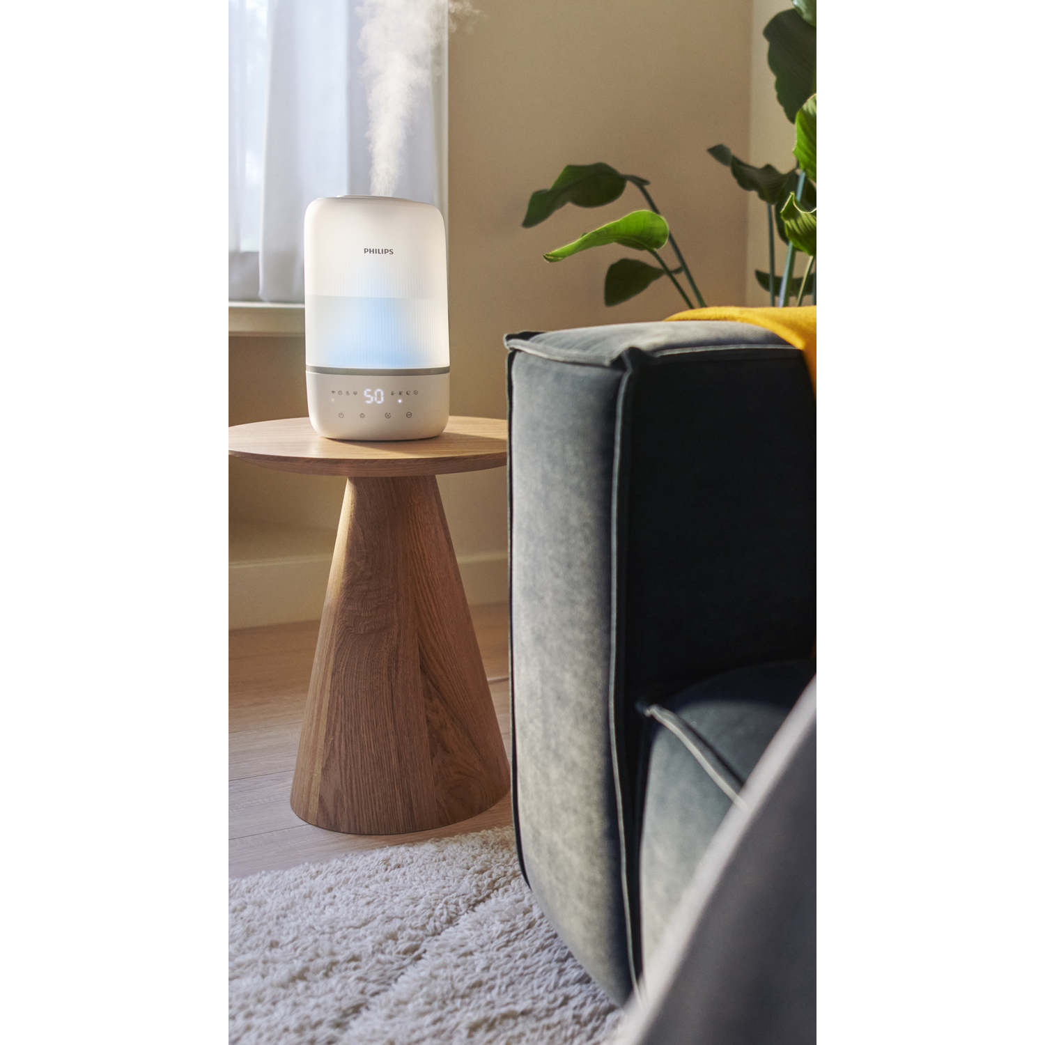 A white humidifier on a wooden table. Steam is coming out. A sofa is behind.