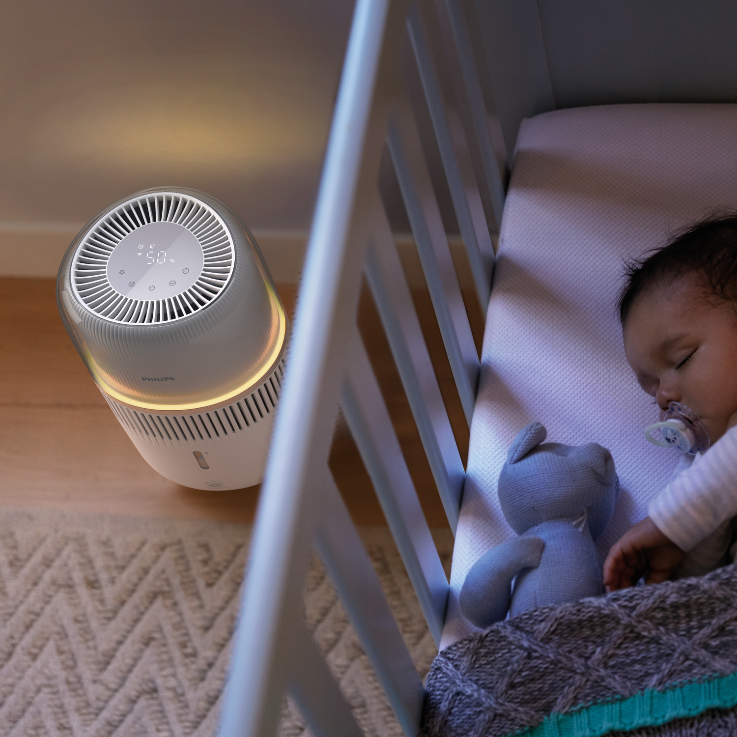 Air purifier next to baby in crib. Baby is sleeping. Humidifier shows display reading 50.
