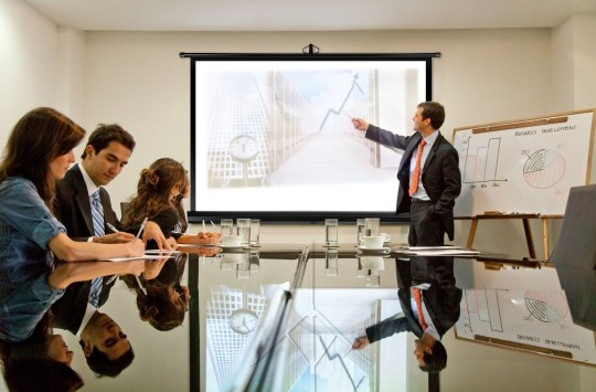 Spotkanie biznesowe w sali konferencyjnej. Mężczyzna prezentuje wykres na ekranie.