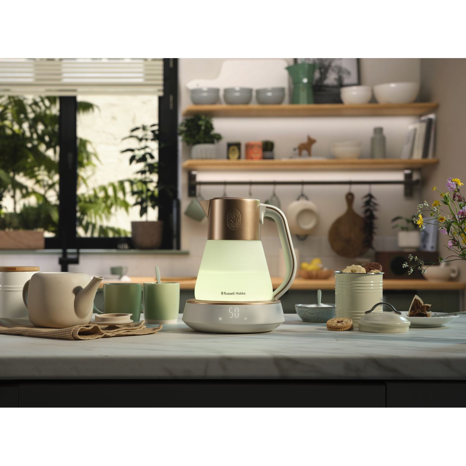 A lit kettle on a base. Tea cups and a teapot are on a counter in a kitchen.