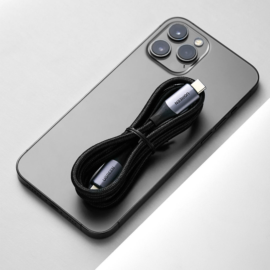 UGREEN markasını sergileyen, koyu renkli bir telefonun üzerine sarılmış siyah örgülü bir USB-C kablosu.