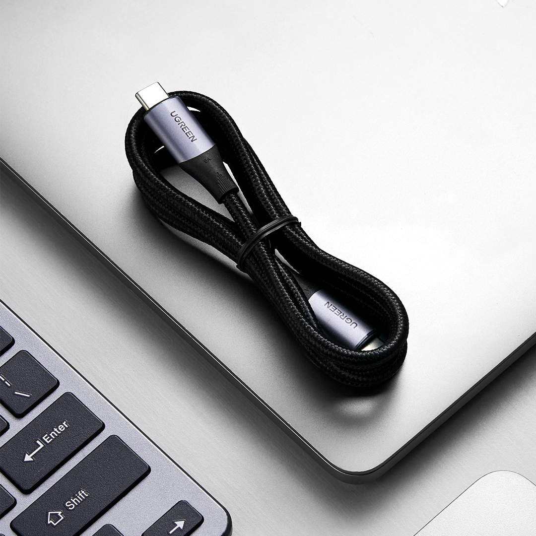 Gri bir dizüstü bilgisayar yüzeyinde düzenli bir şekilde sarılmış siyah bir USB-C kablosu.