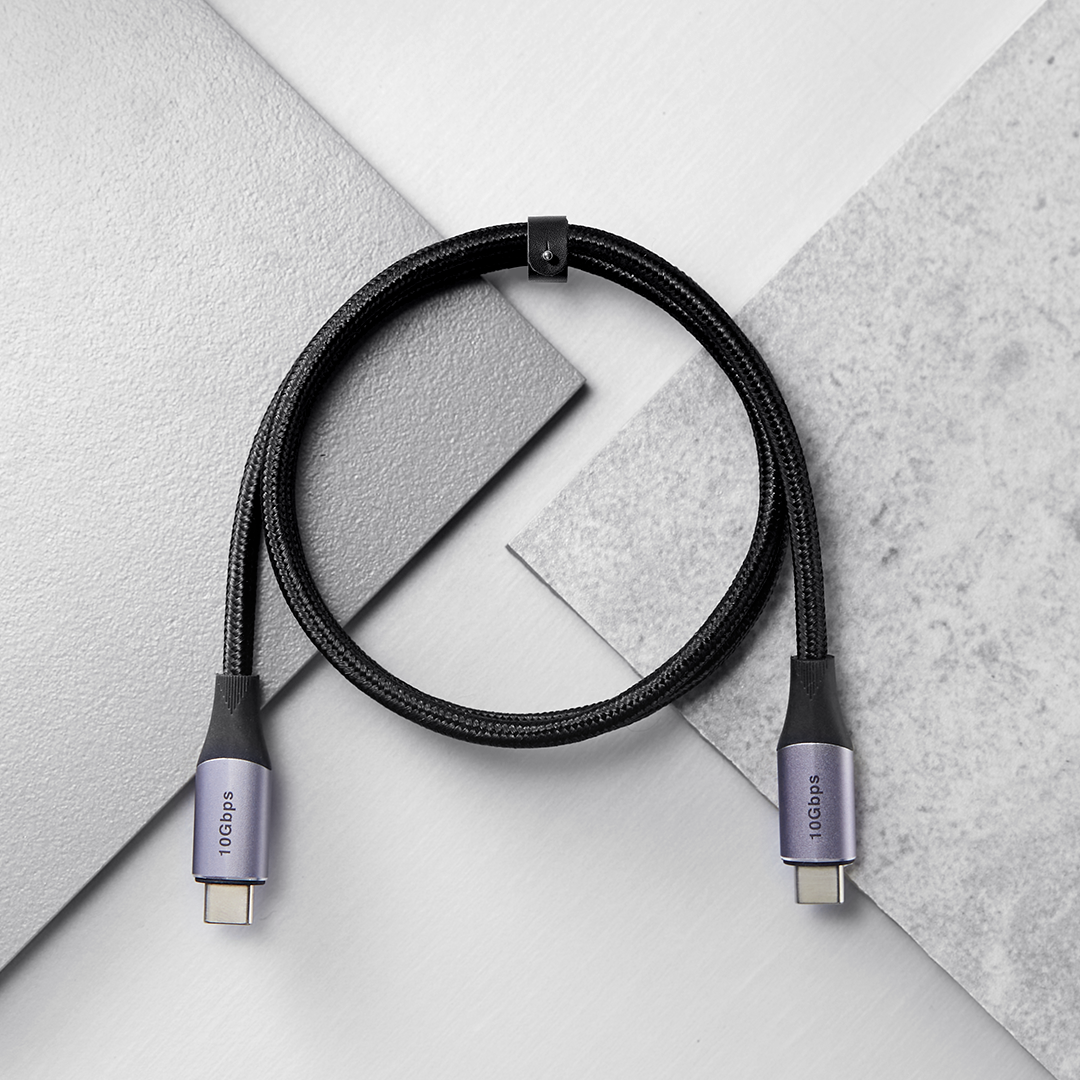 Mor uçlu siyah bir USB-C kablosu, beyaz ve gri desenli bir yüzeyde.