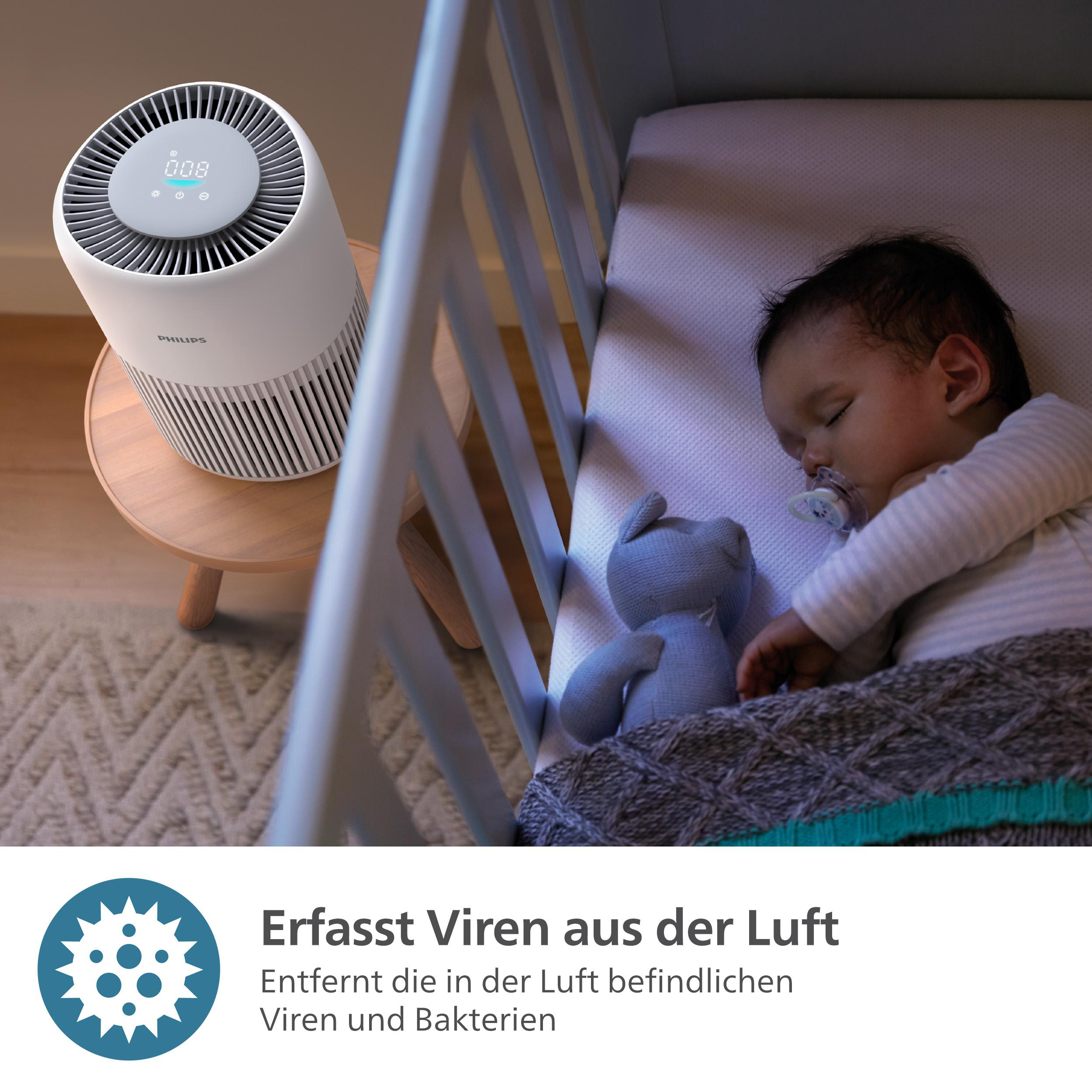 Baby schläft im Kinderbett, ein weißer Luftreiniger steht auf dem Tisch. Der Text lautet 'Erfasst Viren aus der Luft'.