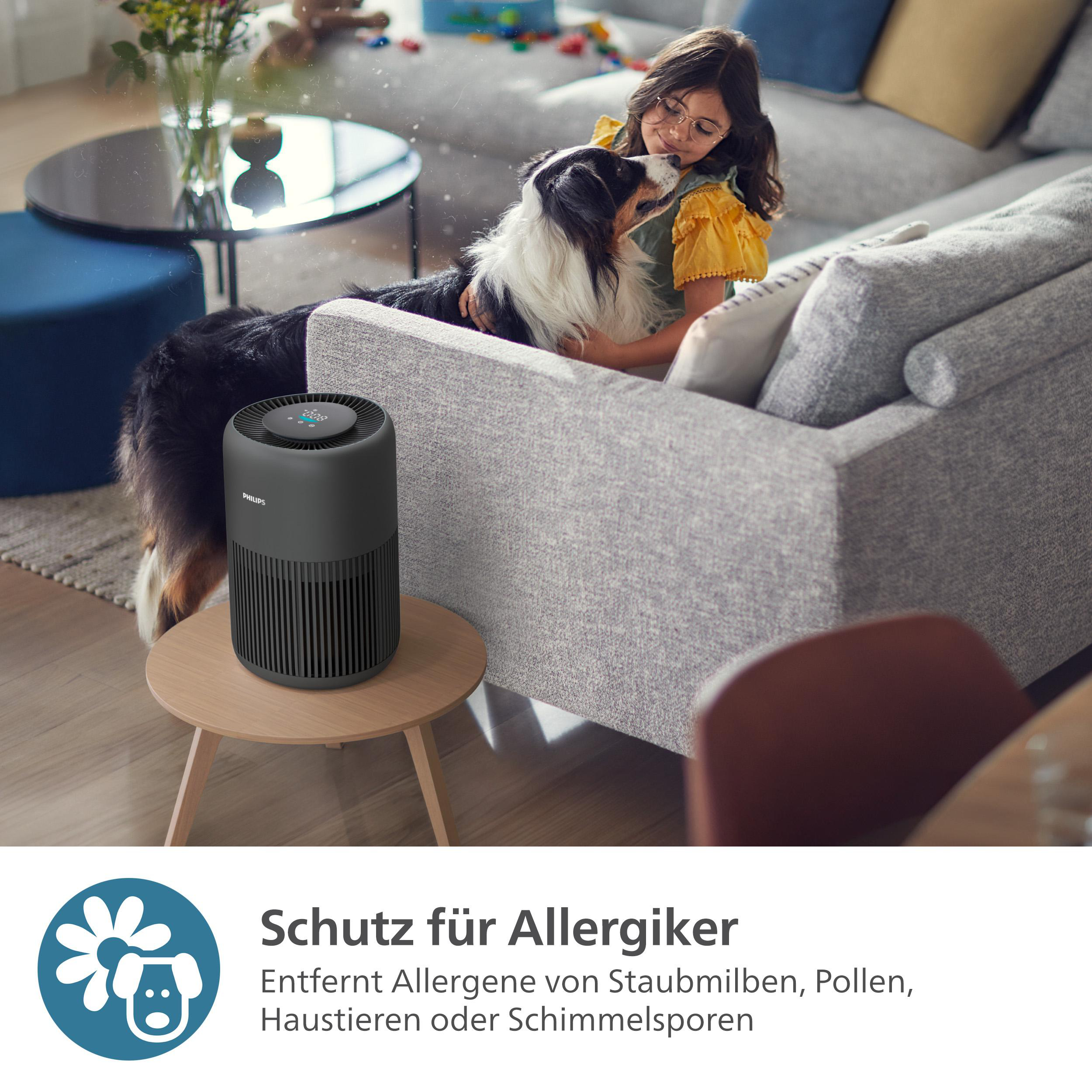 Luftreiniger auf einem Tisch mit Frau und Hund im Hintergrund.