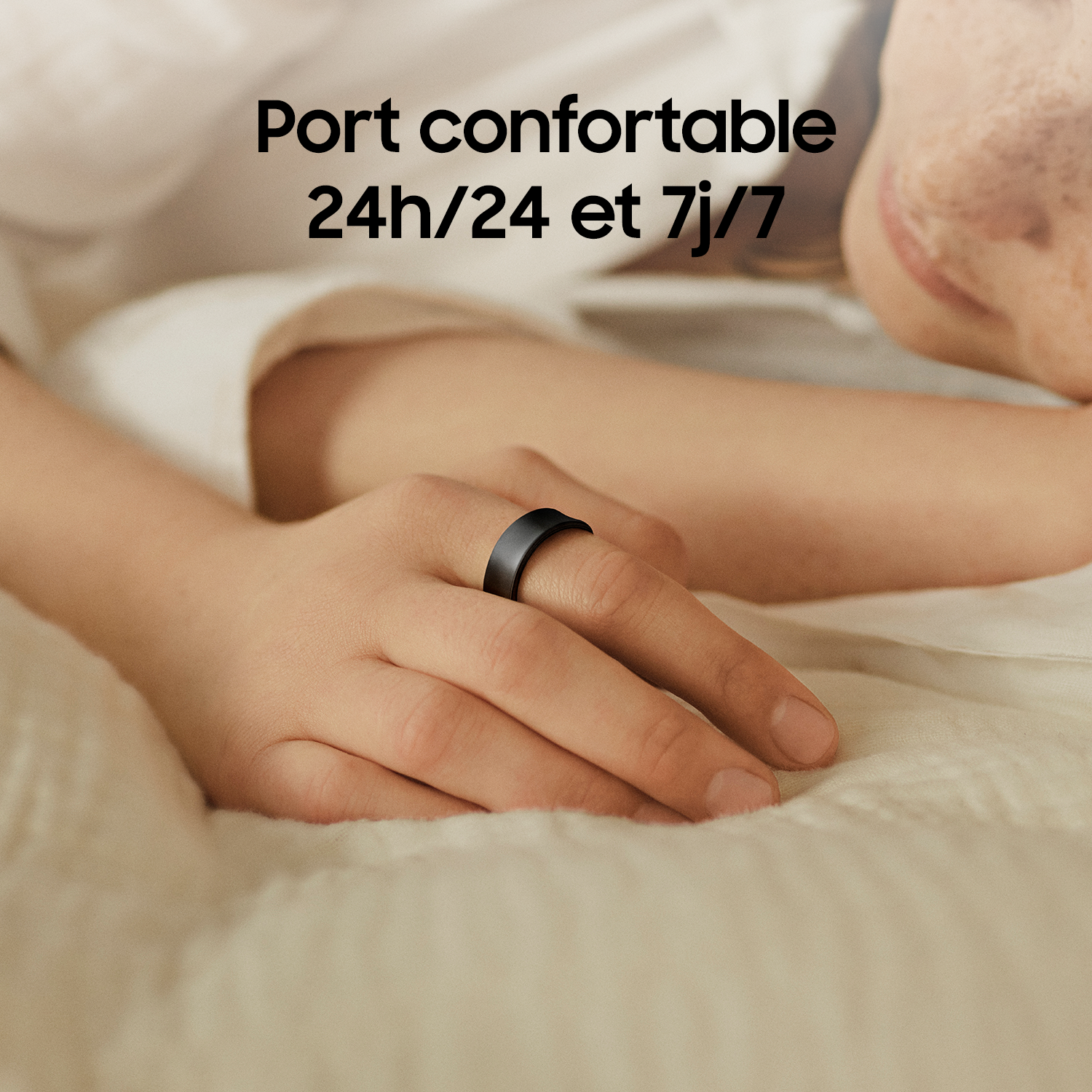 La main d'une personne portant une bague intelligente noire sur un lit.
