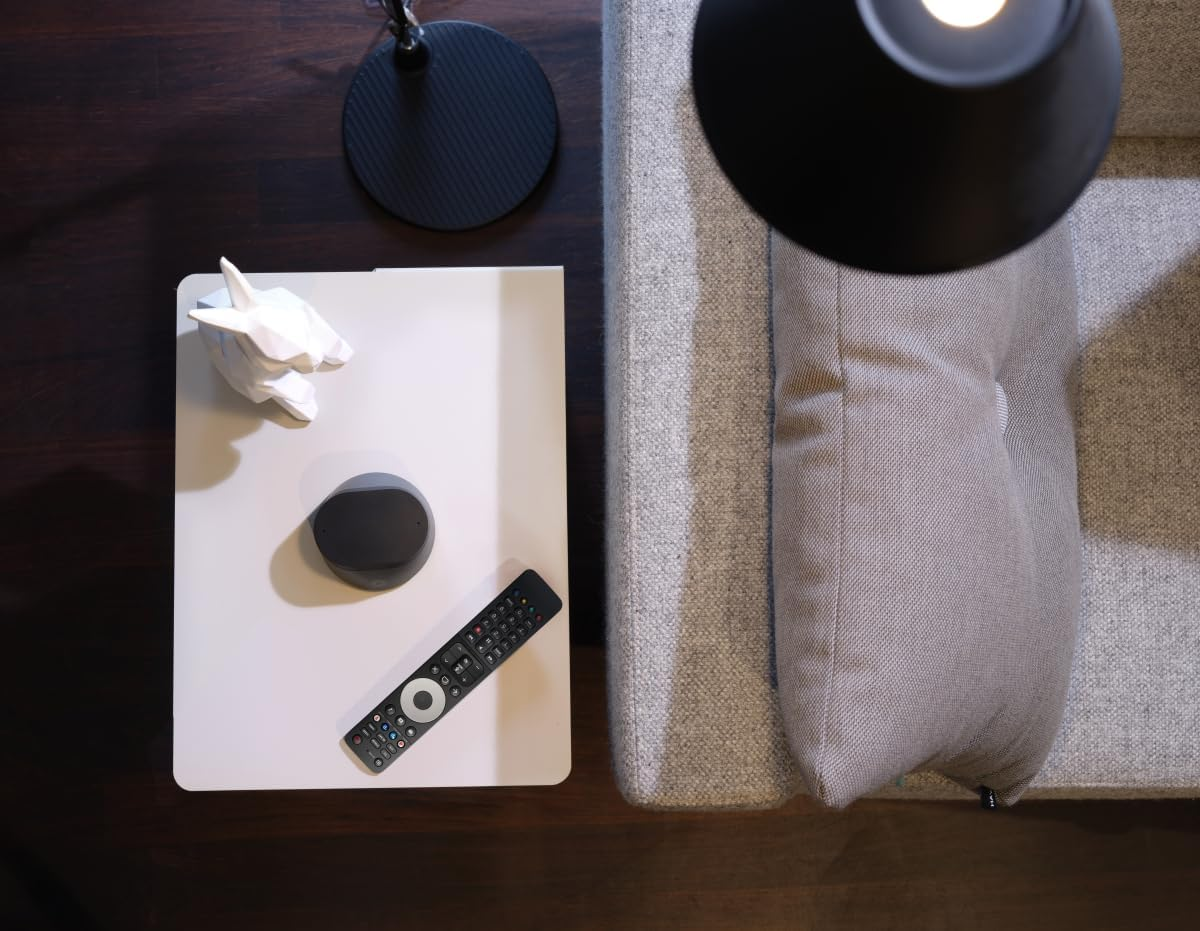 Vue aérienne : table d'appoint blanche avec télécommande, haut-parleur et décoration. Un canapé et une lampe sont également visibles.