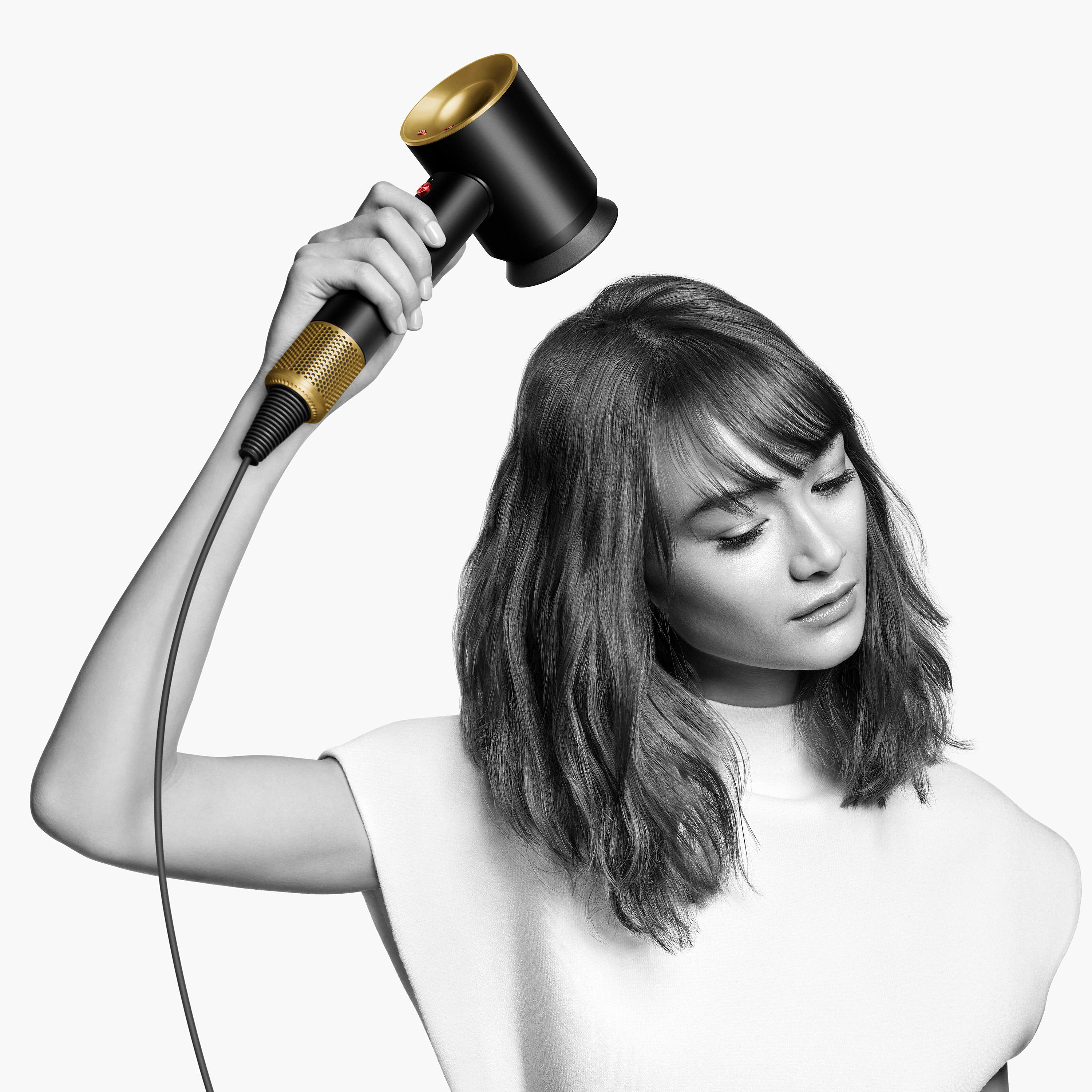 Eine Frau, die nach unten schaut, hält einen schwarzen und goldenen Haartrockner.