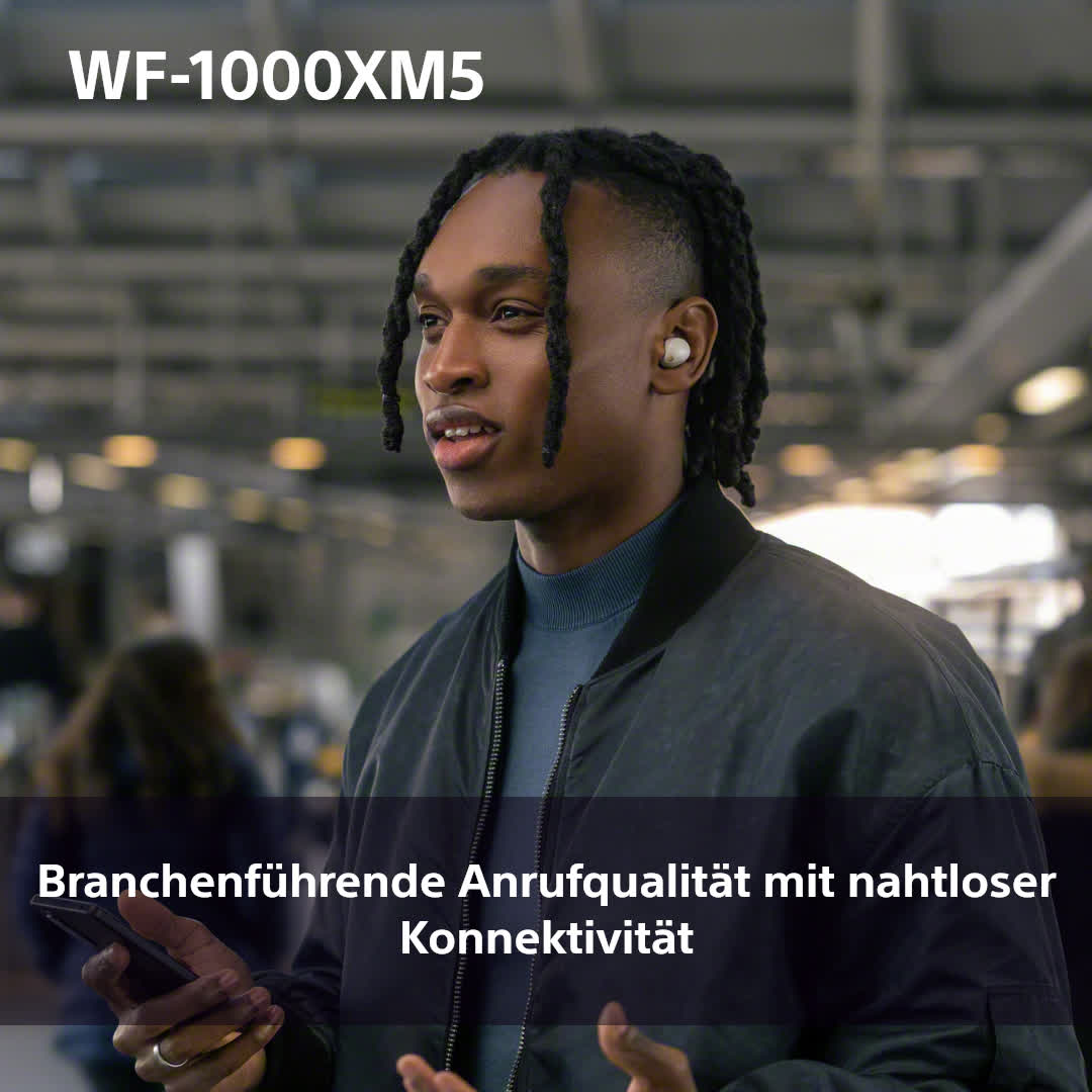 Ein Mann trägt Ohrhörer. Der Hintergrund ist ein geschäftiger Ort.