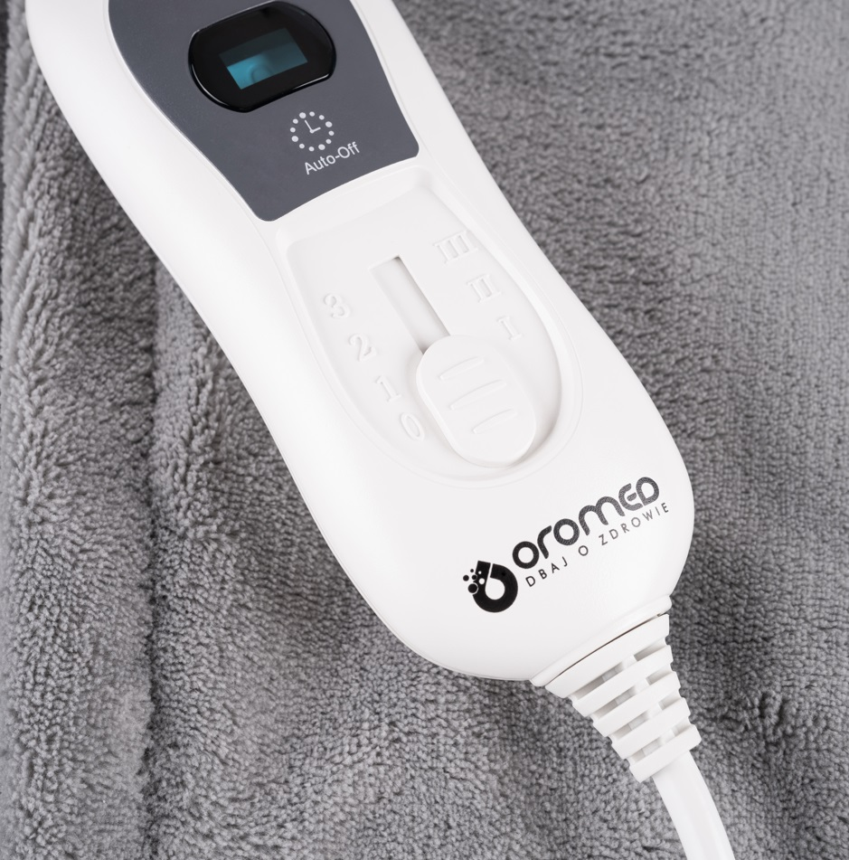 Biało-szary kontroler koca elektrycznego na szarym kocu. Ma przyciski i pokrętło.