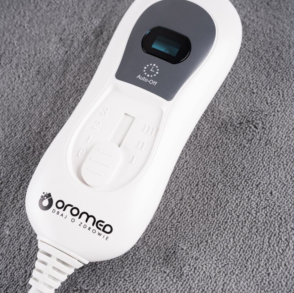 Panel sterowania podkładki grzewczej na szarym ręczniku.