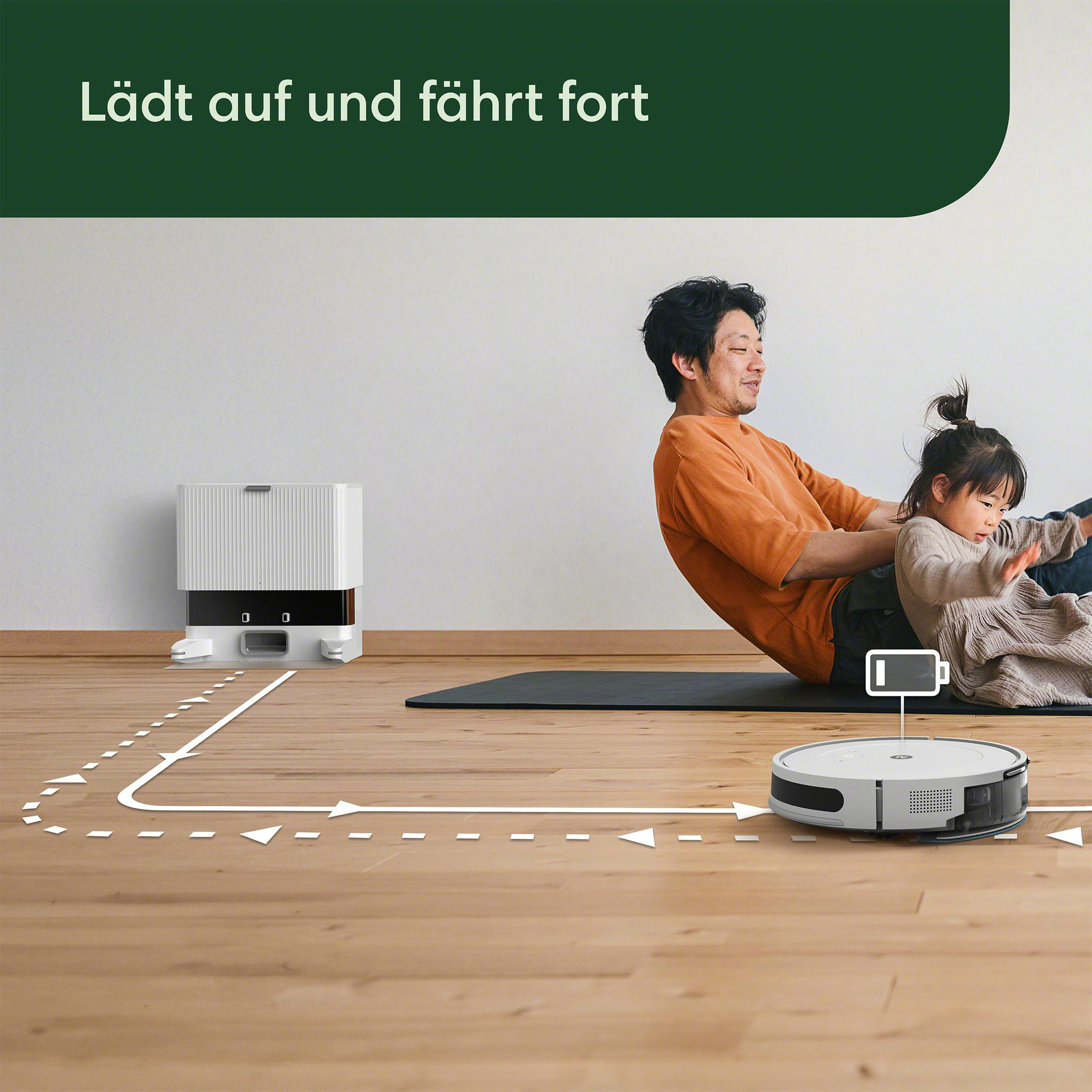 Ein Mann und ein Kind sitzen auf dem Boden. Ein Roboter-Staubsauger arbeitet auf dem Holzboden.